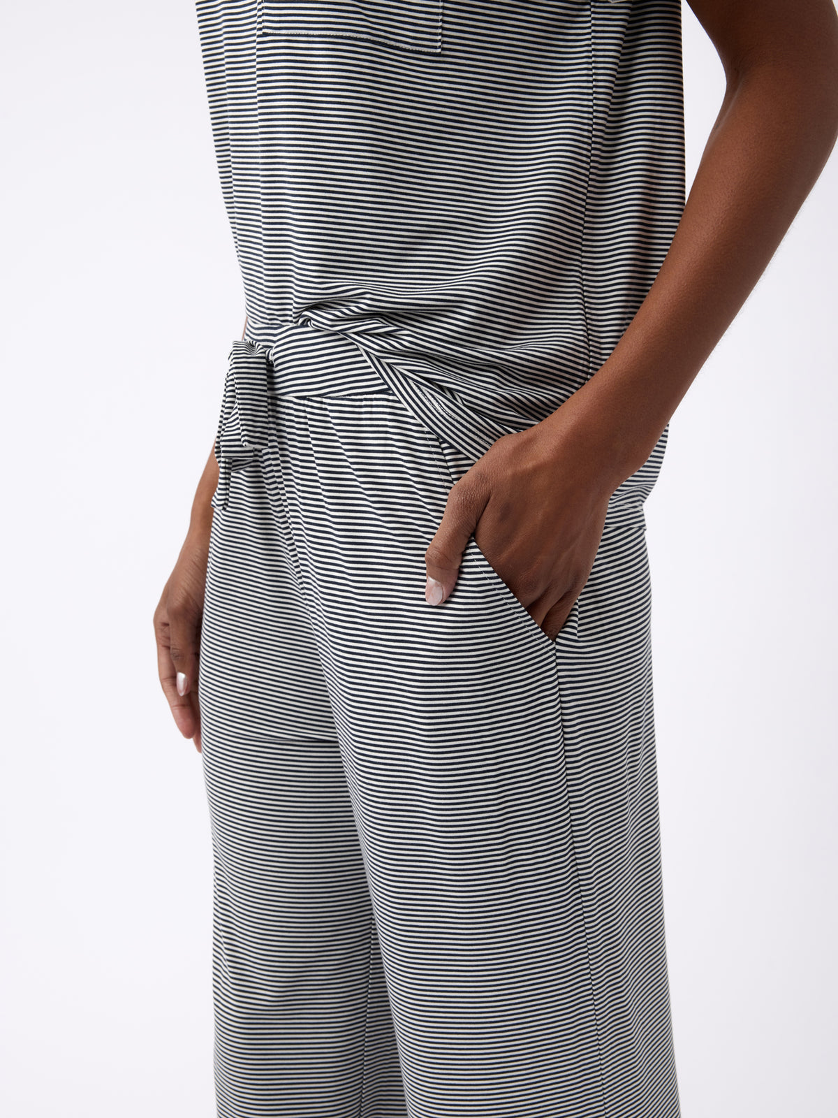 A person is wearing a Cozy Earth Women's Bamboo Stretch-Knit Pant, featuring a gray striped design, short-sleeved pocket shirt, and pants with a waist tie detail. Their hand rests in the pant pocket. 