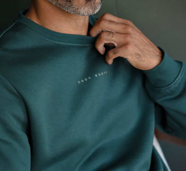 Person wearing a teal sweatshirt with 'Cozy Earth' logo, touching their neck.
