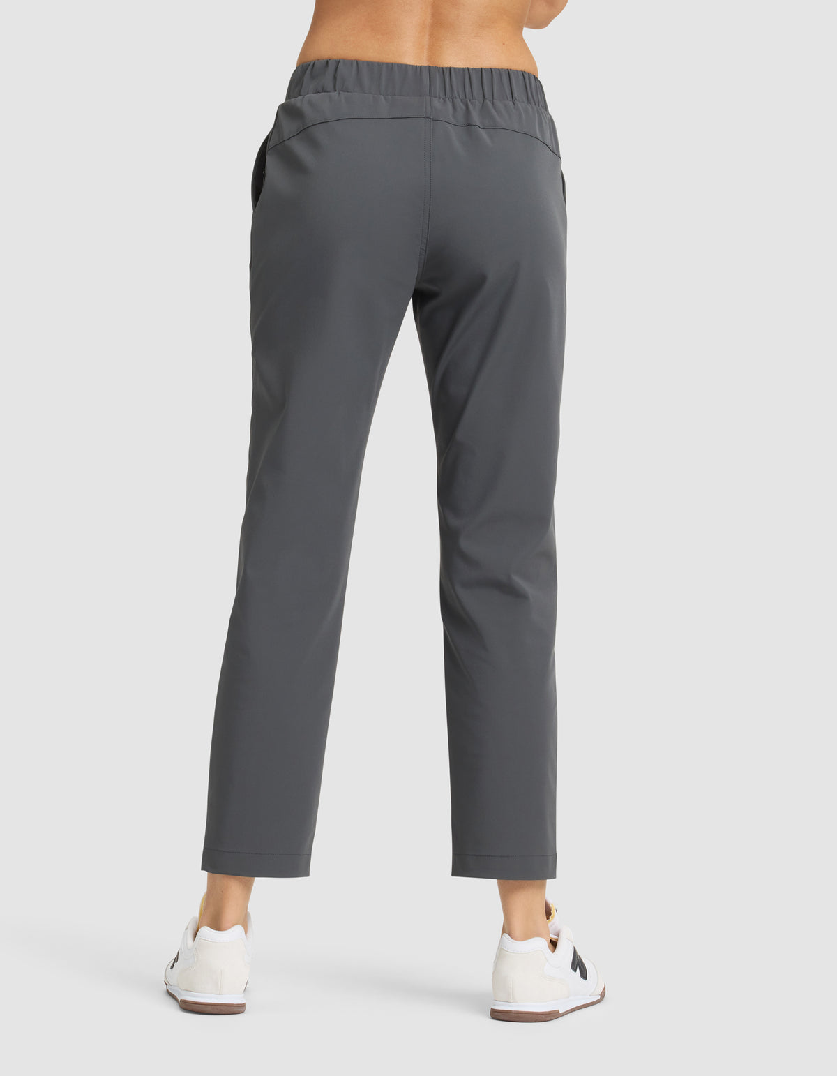 A person faces away, wearing Cozy Earth's Women's Always Cropped Pant in gray with an elastic waistband, paired with white sneakers on a plain light background. 