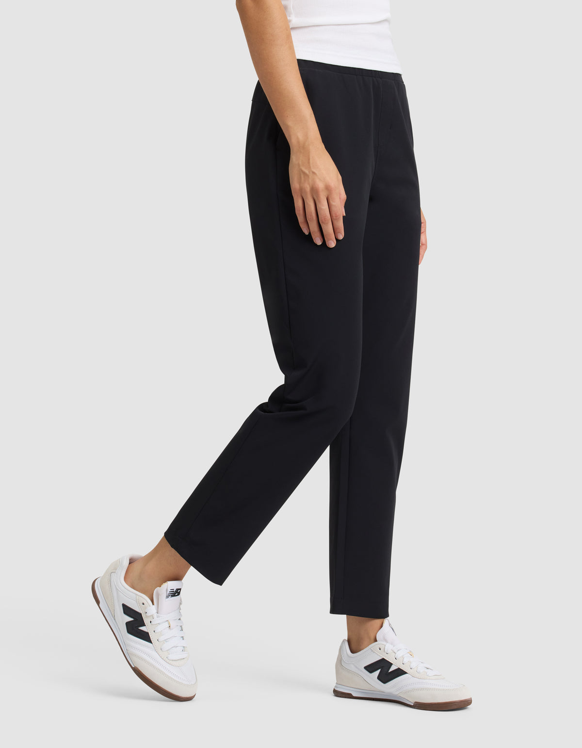 A person wearing Cozy Earth's Women's Always Cropped Pant in black, a white top, and white sneakers stands against a plain light gray background. Only the lower torso and legs are visible. 