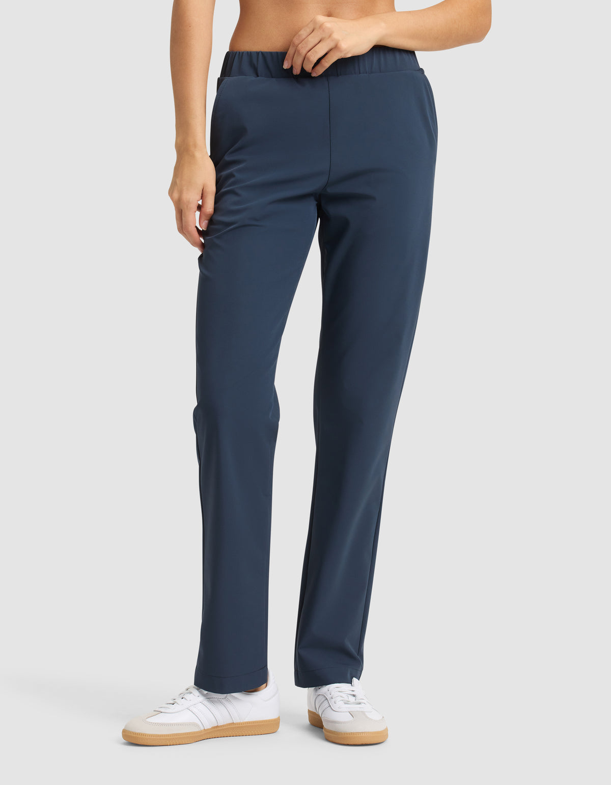 A woman in Cozy Earth's Women's Always Pant, navy blue with a straight-leg cut and elastic waistband, paired with white sneakers, stands against a plain light background. 