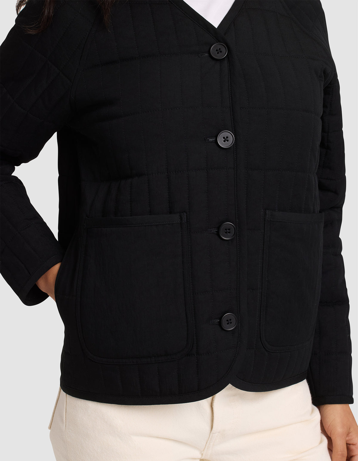 A woman is shown from shoulders to hips wearing the Cozy Earth Women's Andie Quilted Jacket in black, featuring two large front pockets, paired with light-colored pants.