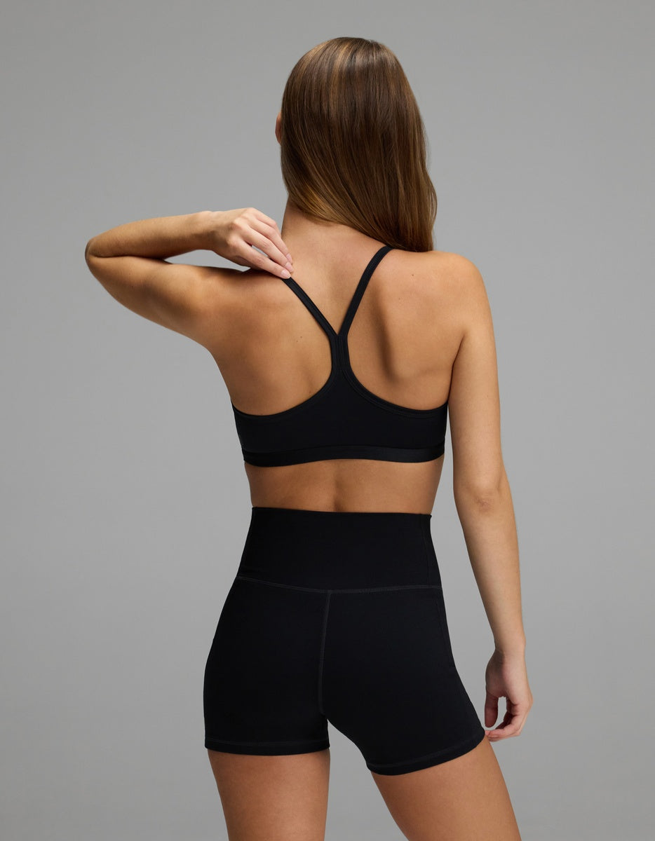 A person seen from behind, wearing a black Cozy Earth Women’s Balance Bra with racerback straps and high-waisted black shorts.