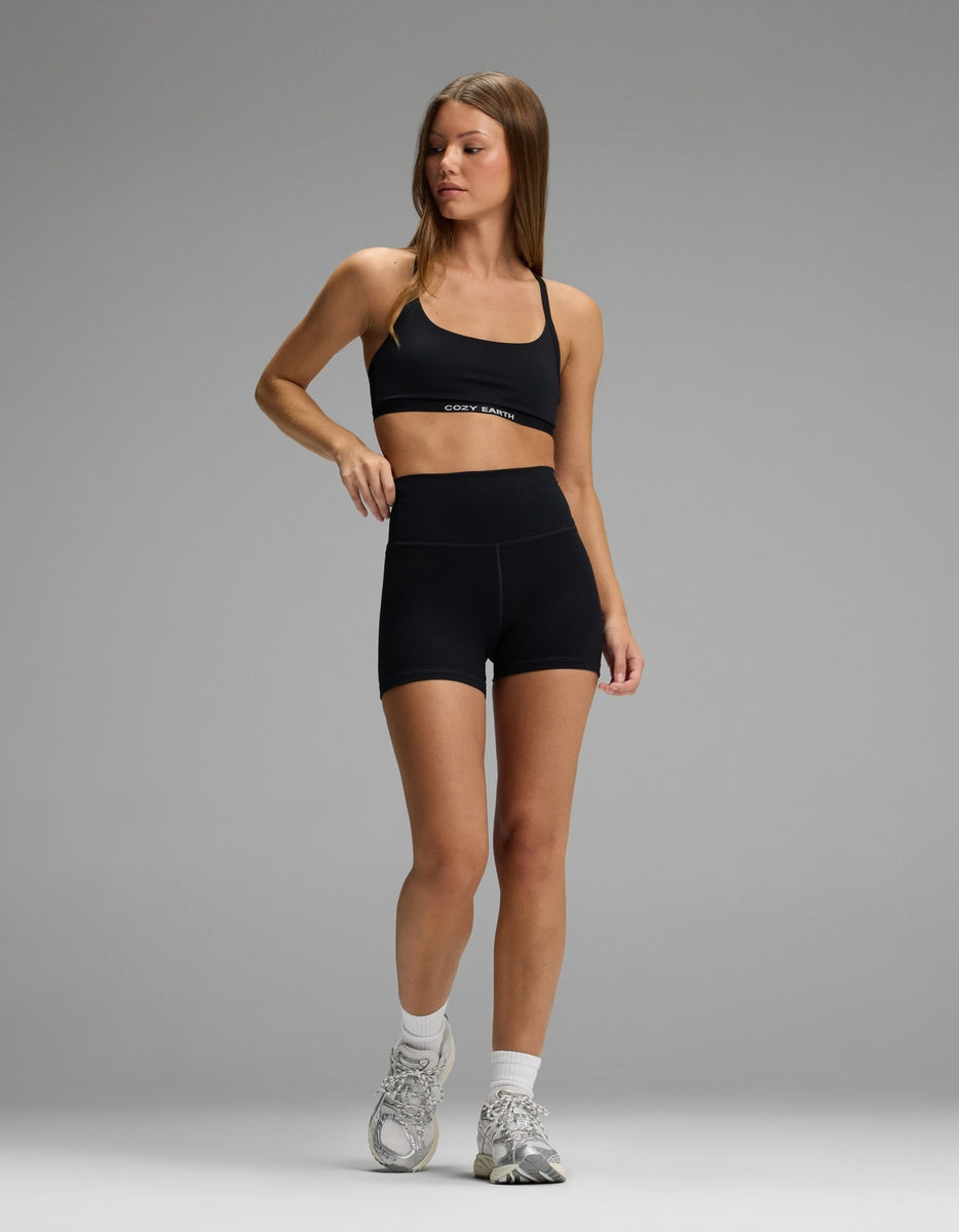 A woman wearing a black Cozy Earth Women’s Balance Bra with matching high-waisted shorts, white socks, and athletic sneakers.