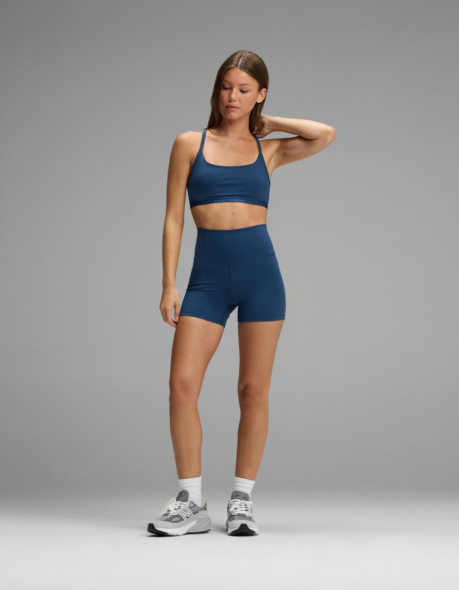 A person wearing a dark blue Cozy Earth Women’s Balance Bra and matching high-waisted shorts with gray sneakers.