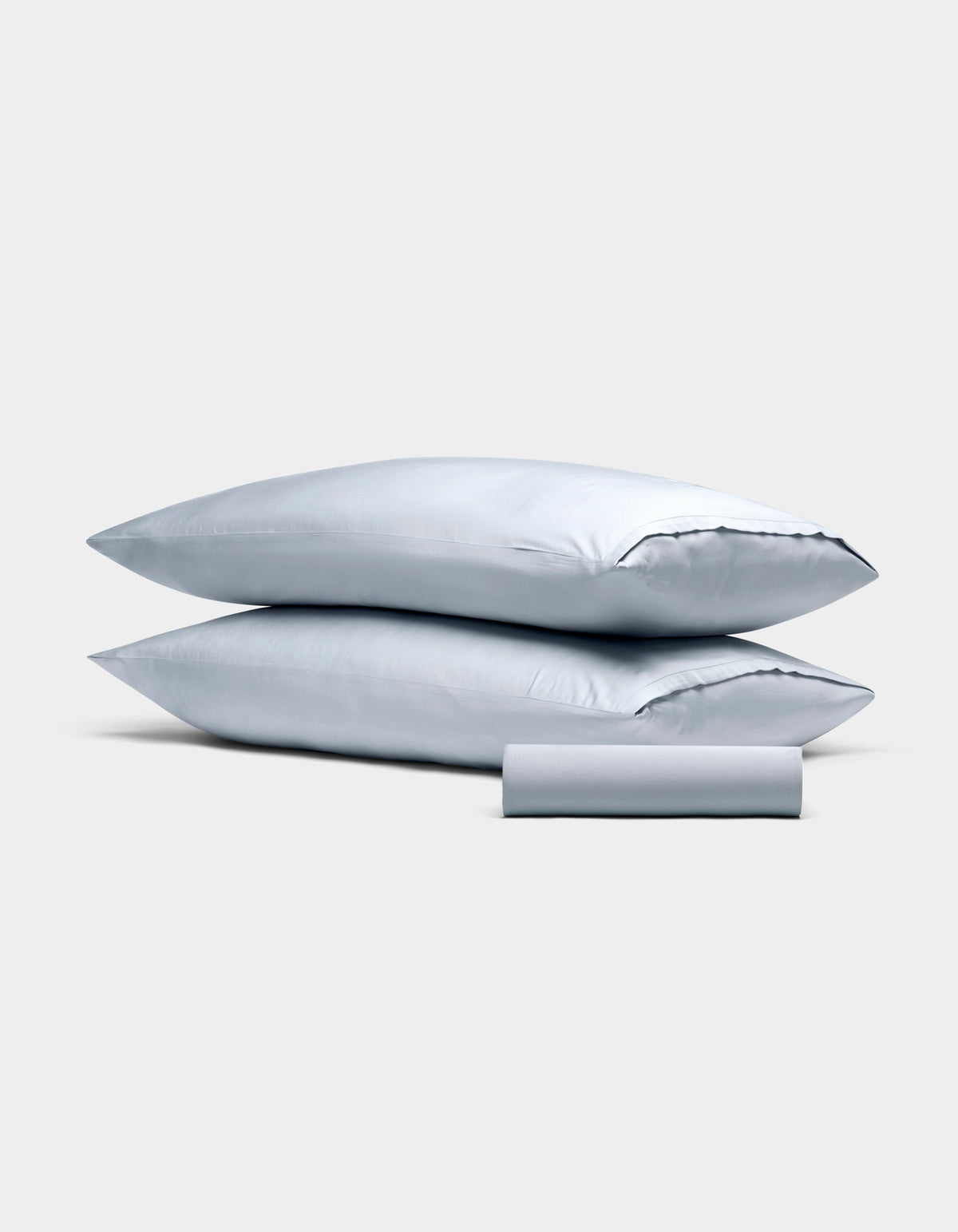 The Bamboo Bedding Basic Bundle by Cozy Earth features two light gray pillowcases stacked together and a matching rolled-up fabric piece in front, all displayed against a plain light gray background.|Color:Shore