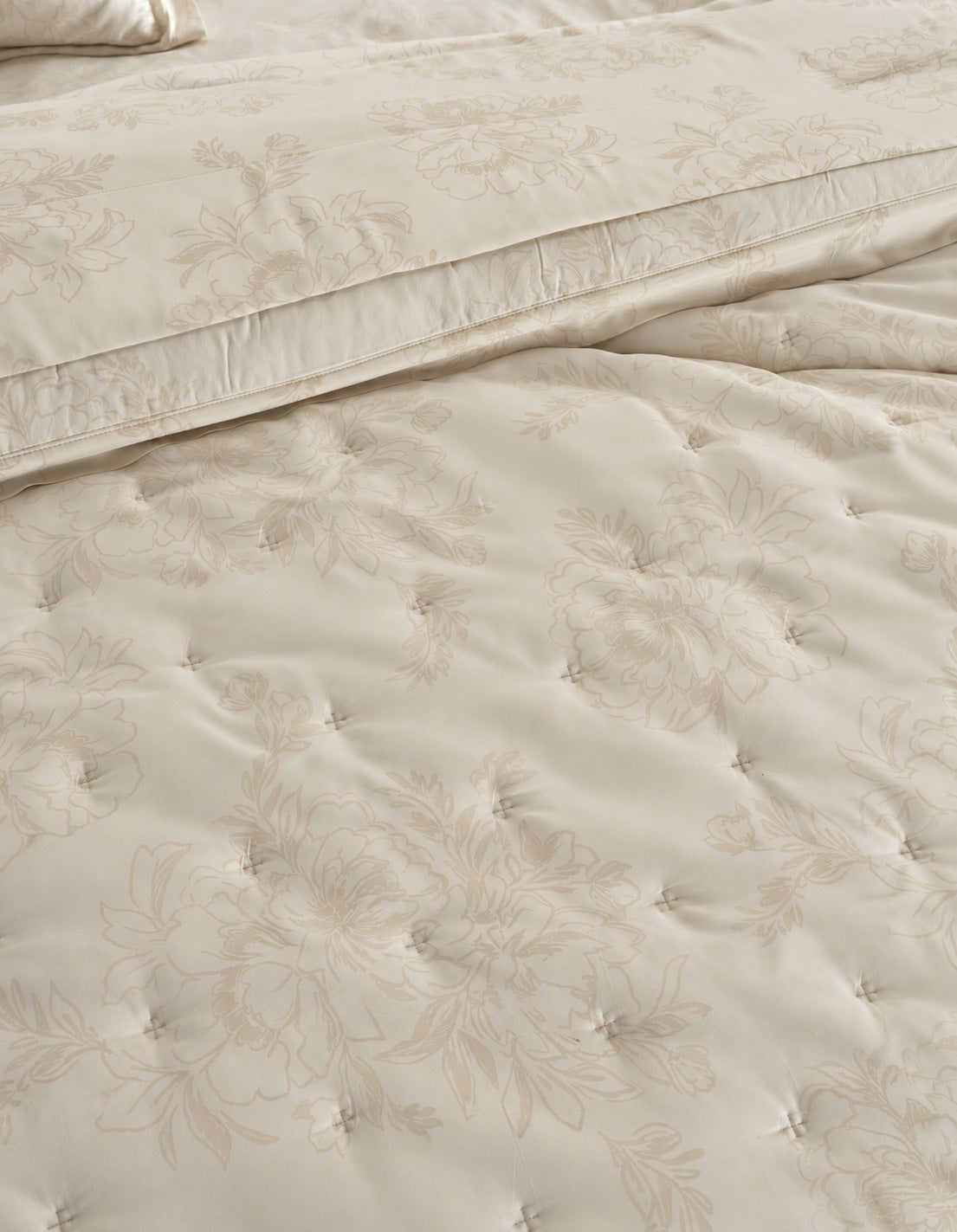 Close-up of a cream-colored quilted bedding set with a subtle floral jacquard pattern, showing the texture of the tufted comforter and matching pillowcase. |Color:Sonoma Floral in Vintage White