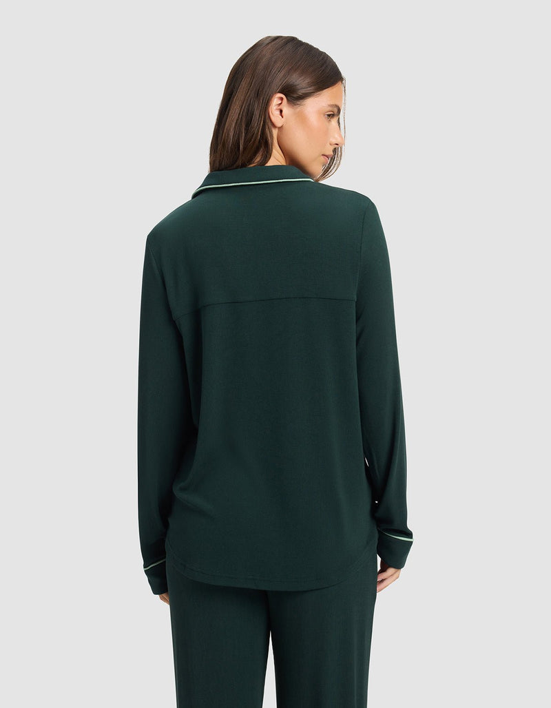 A woman with straight brown hair is seen from behind, wearing a Cozy Earth Women's Bamboo Rib-Knit Classic Long Sleeve Pajama Top in dark green with matching pants against a plain light gray background.