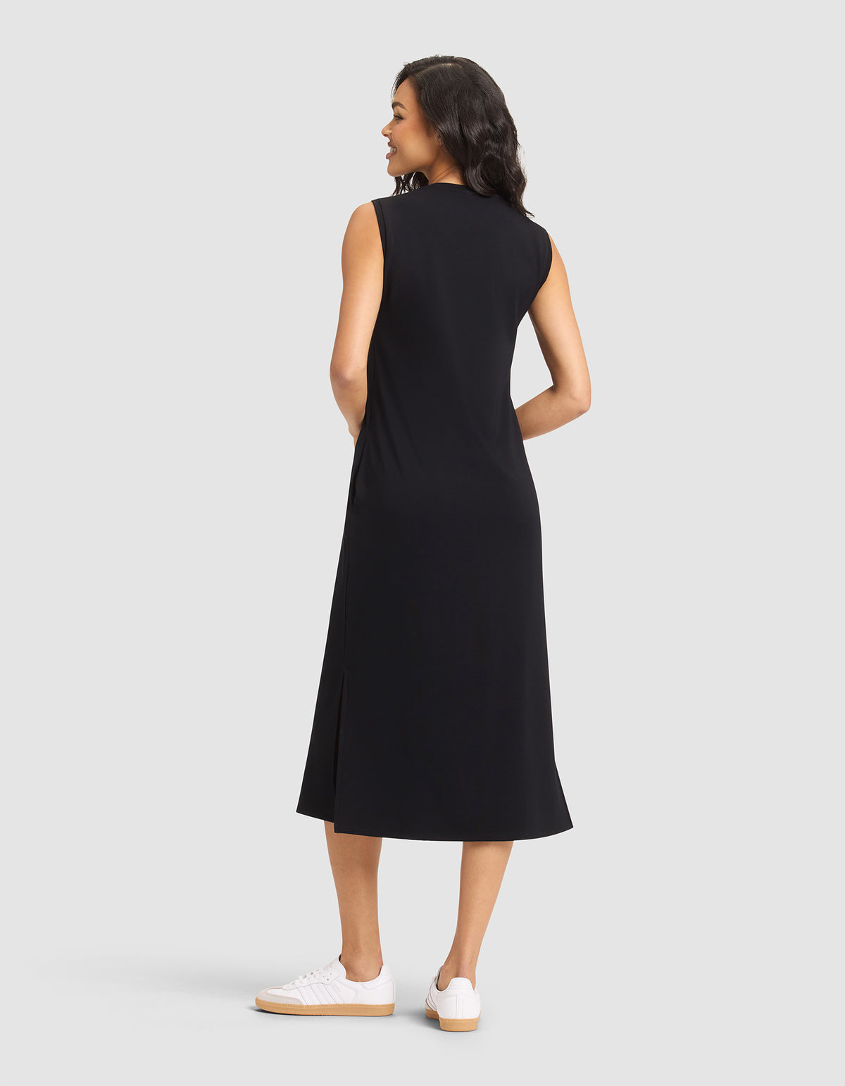 A woman with dark, wavy hair smiles while wearing the Cozy Earth Women's Brushed Bamboo Sleeveless Midi Dress in black and white sneakers, standing against a plain light gray background. 