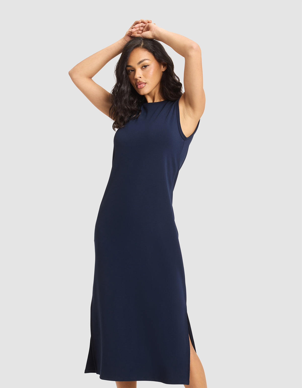 A woman wears the Cozy Earth Women's Brushed Bamboo Sleeveless Midi Dress in navy, standing against a plain light background with her arms raised and hands clasped. 