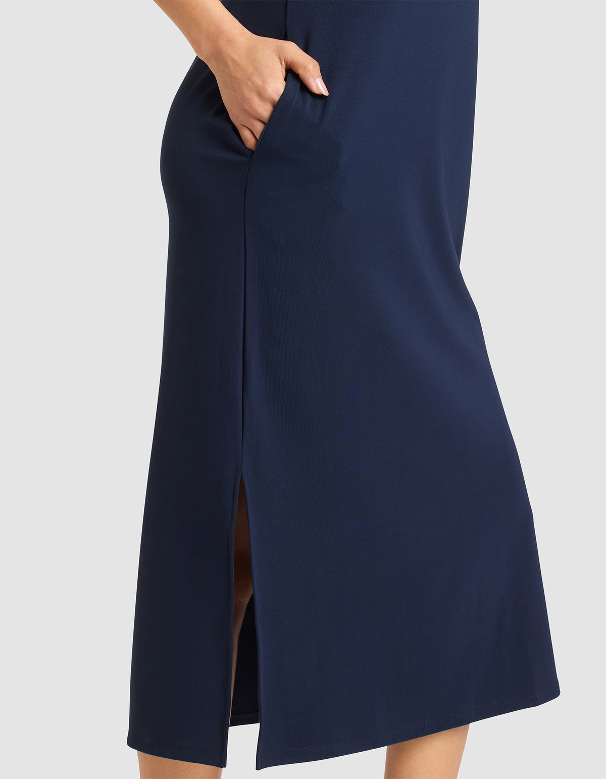 The lower half of a person is shown wearing the Cozy Earth Women's Brushed Bamboo Sleeveless Midi Dress in navy blue, featuring a side pocket and side slit, standing against a light gray background. 