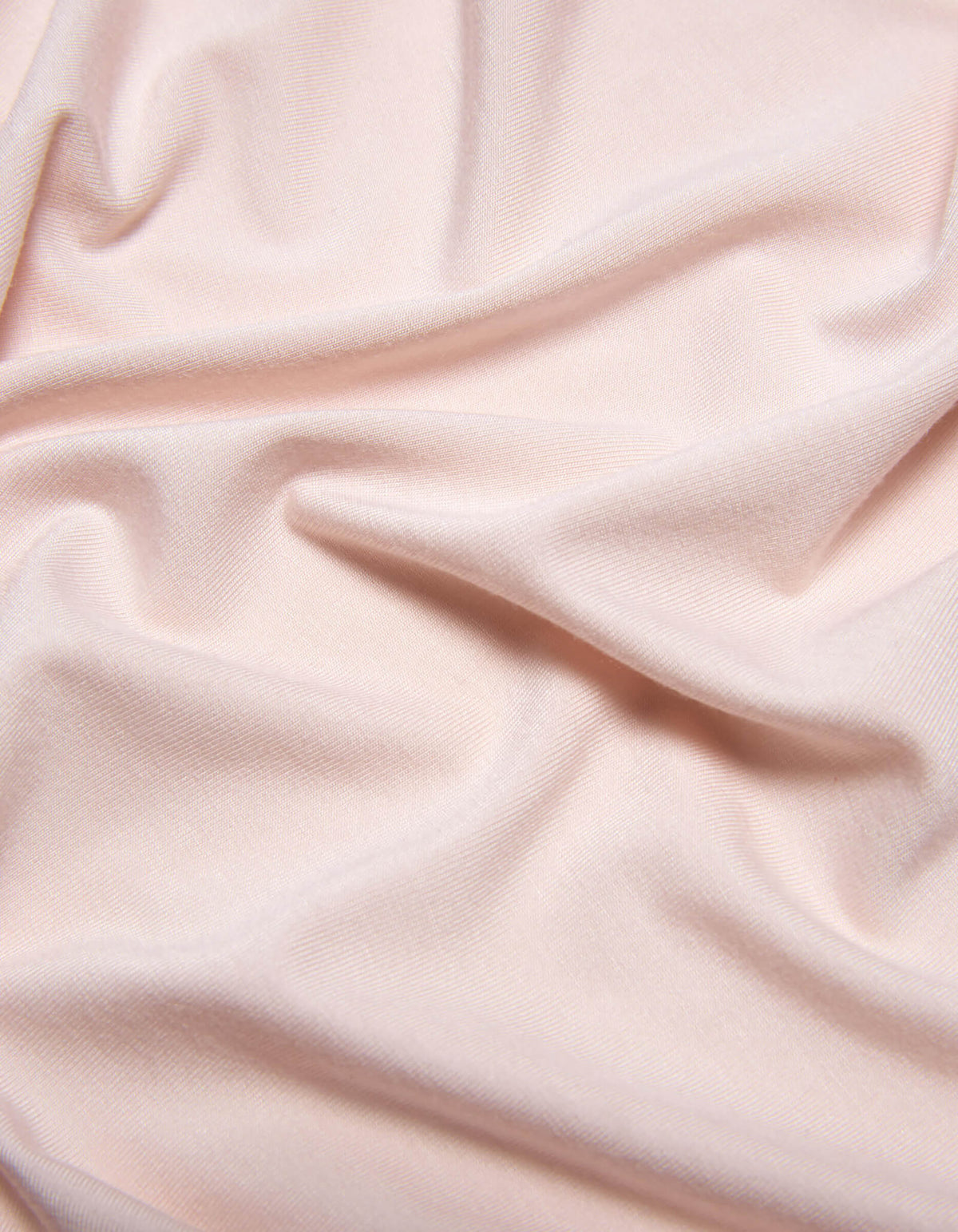 The Bamboo Jersey Sheet Set by Cozy Earth features soft, light pink fabric with subtle folds and gentle wrinkles for a smooth, slightly textured look.
