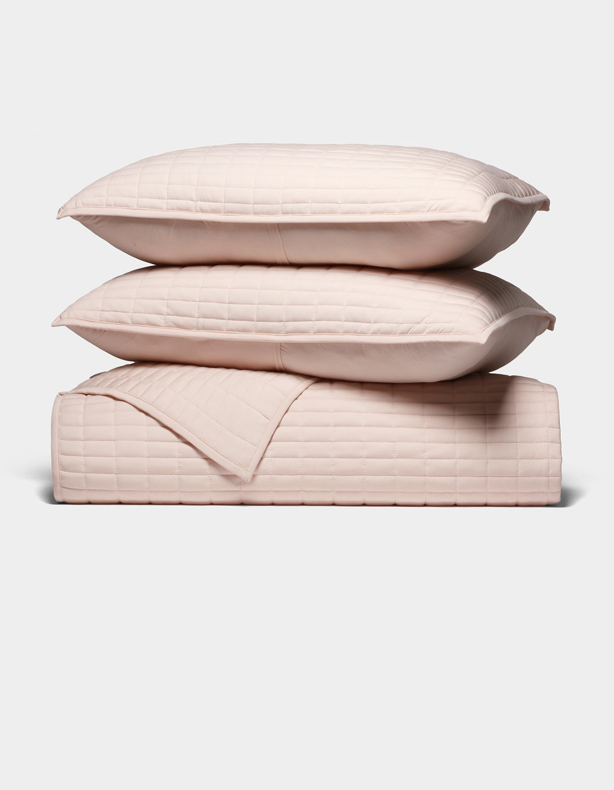 The Cozy Earth Bamboo Jersey Quilt Bundle features two light pink quilted pillows stacked atop a matching quilted blanket, all neatly arranged against a plain white background.