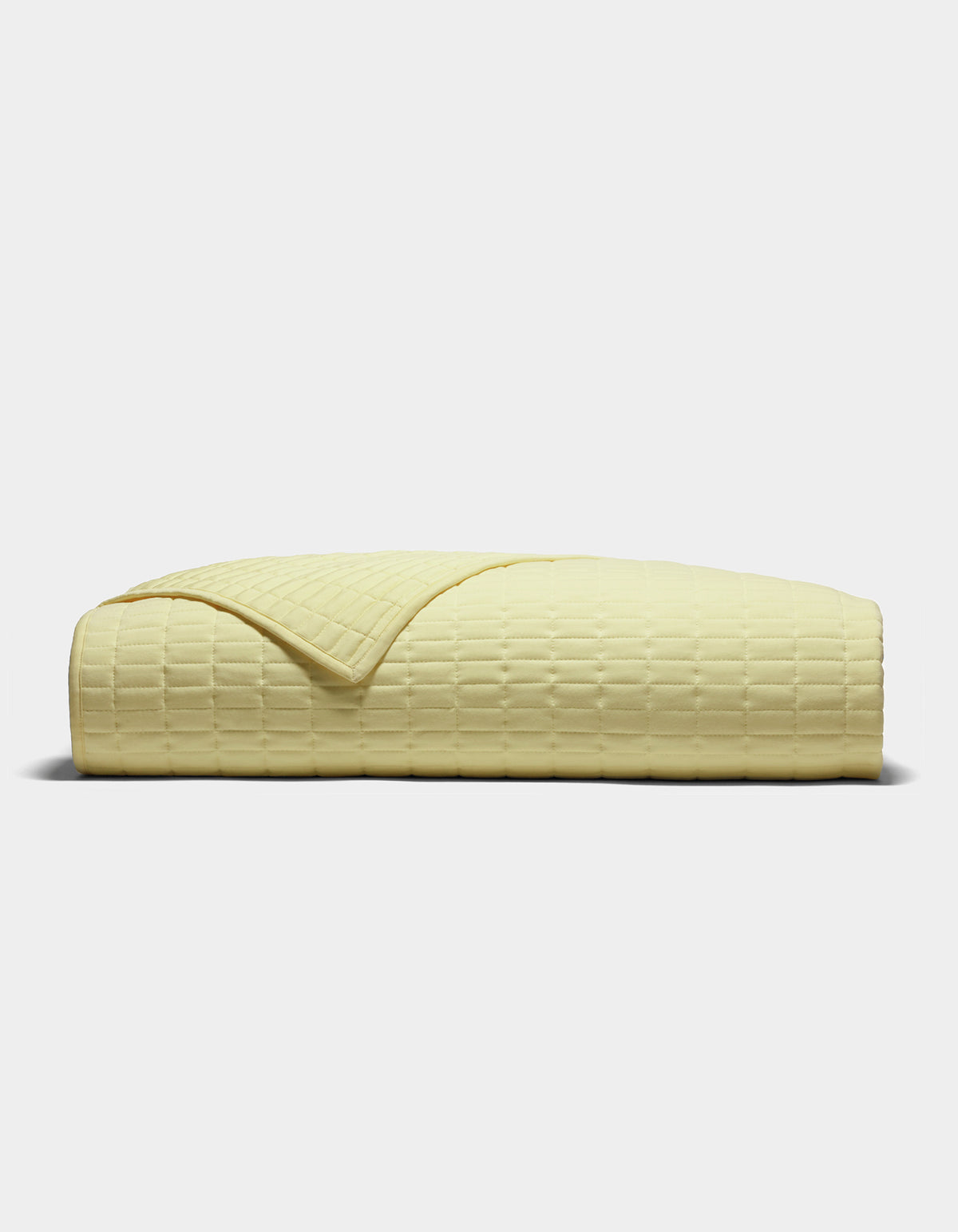 The Cozy Earth Bamboo Jersey Quilt, shown folded from the side on a plain light background, features a pale yellow color and a subtle grid-like textured pattern.