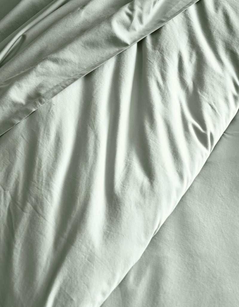 The Soft-Wash Cotton Duvet Cover by Cozy Earth features a light gray finish with subtle wrinkles and gentle folds, creating soft shadows across the fabric.