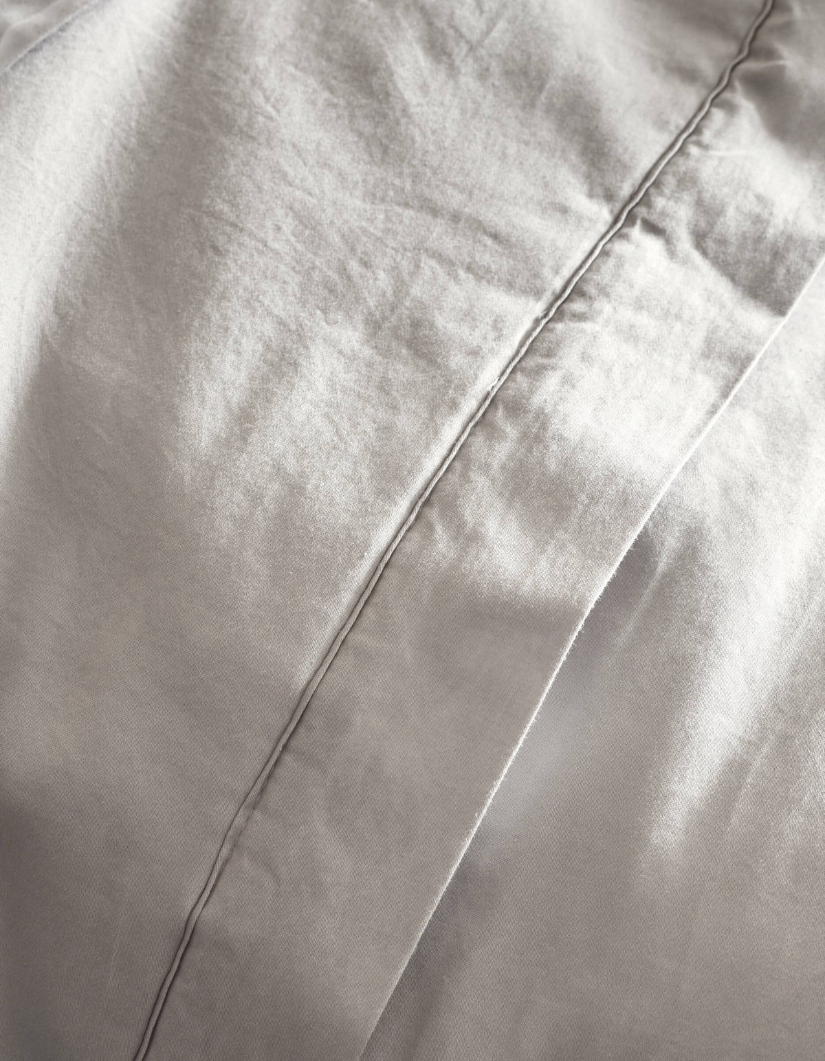 Close-up of Cozy Earth’s Soft-Wash Cotton Quilt in light gray, featuring a prominent vertical stitched seam, gentle folds, and a smooth, soft texture.