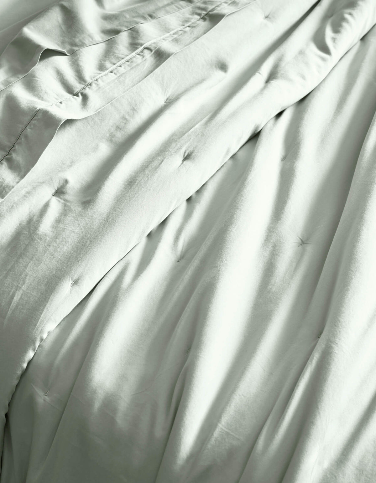 Close-up of Cozy Earth’s Soft-Wash Cotton Quilt, showcasing its light color, gentle folds, and subtle tufted details for a soft, comfortable, and inviting bed.
