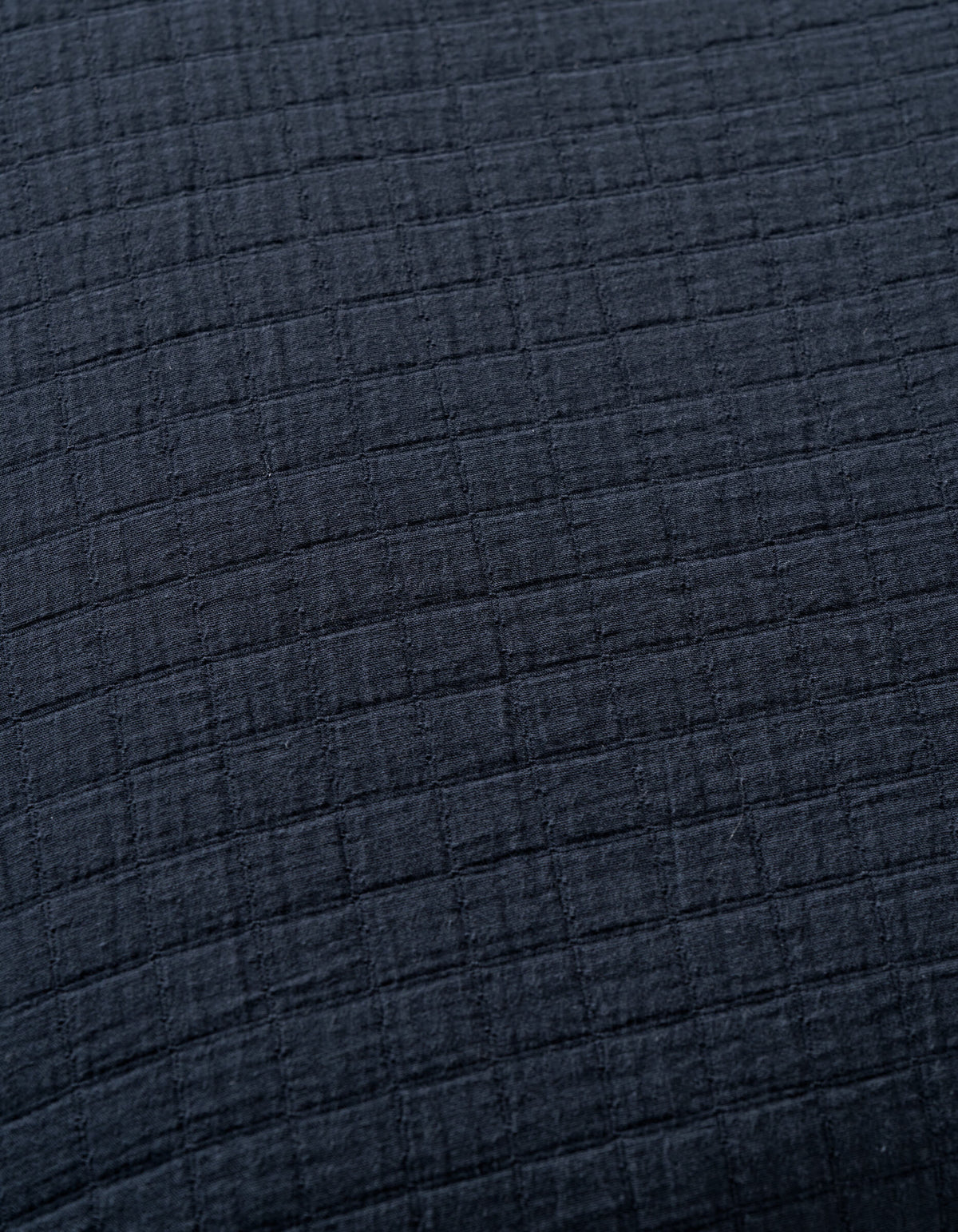 Close-up of Cozy Earth's Waterfront Grid Matelasse Blanket in dark gray or black, featuring a soft textured fabric with a subtle grid pattern formed by raised horizontal and vertical lines.