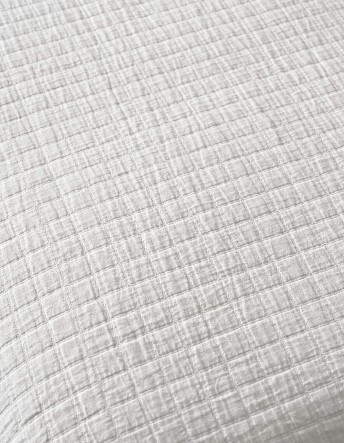 A close-up of Cozy Earth's Waterfront Grid Matelasse Blanket, featuring white fabric with a subtle checkered texture, small raised squares, and soft, crinkled material.