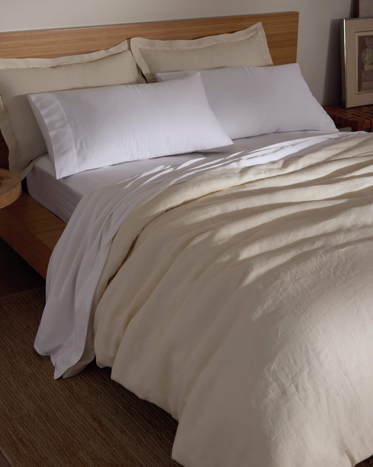 A bed features the Cozy Earth Linen Duvet Cover, white pillows, and a wooden headboard. A bedside table adds warmth to the softly lit room, creating a cozy and inviting atmosphere.