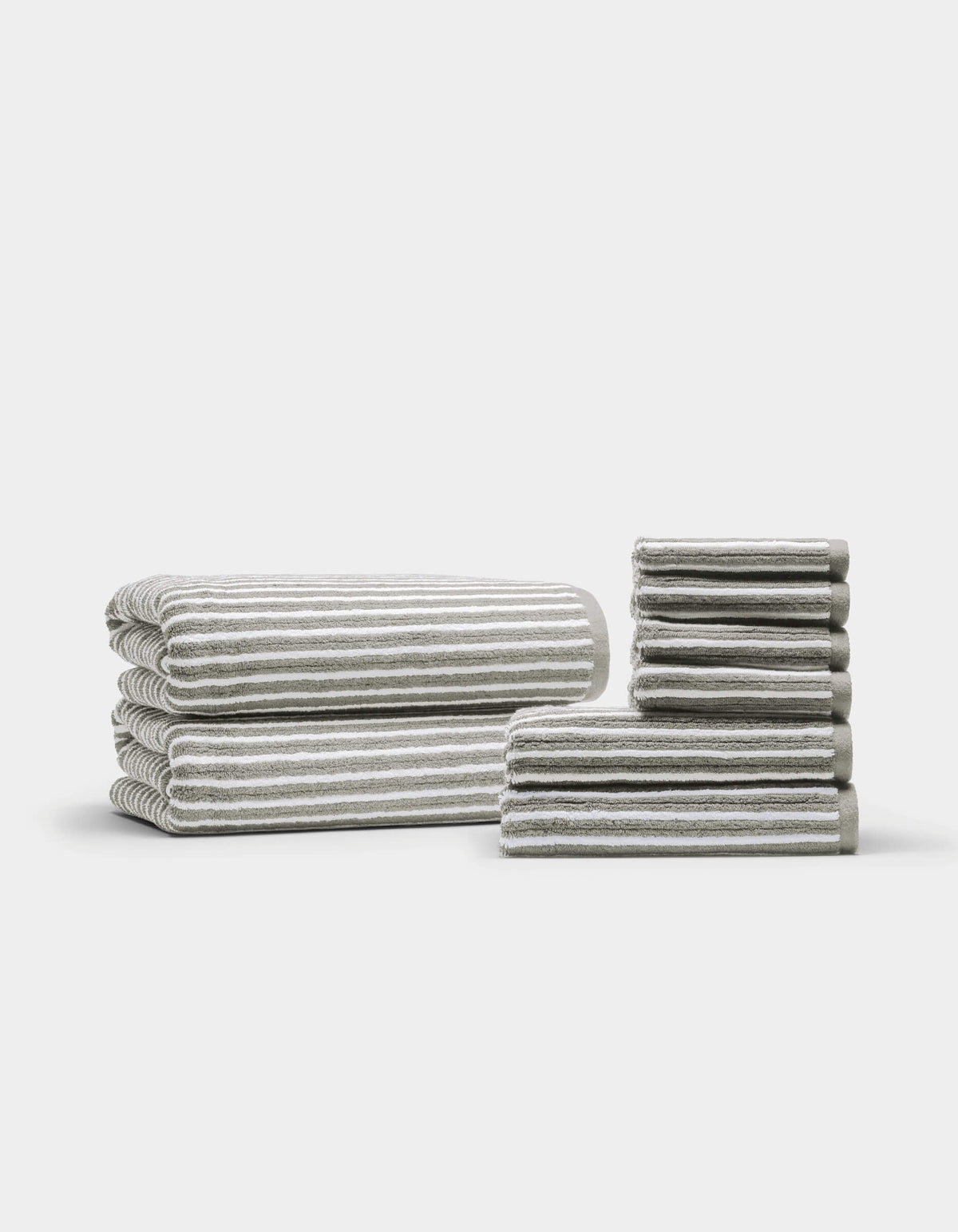 Two neatly arranged stacks of the Cozy Earth Ribbed Terry Bath Towel Set are displayed on a plain white background—one larger stack featuring bath towels, and a smaller stack showcasing hand towels and washcloths.