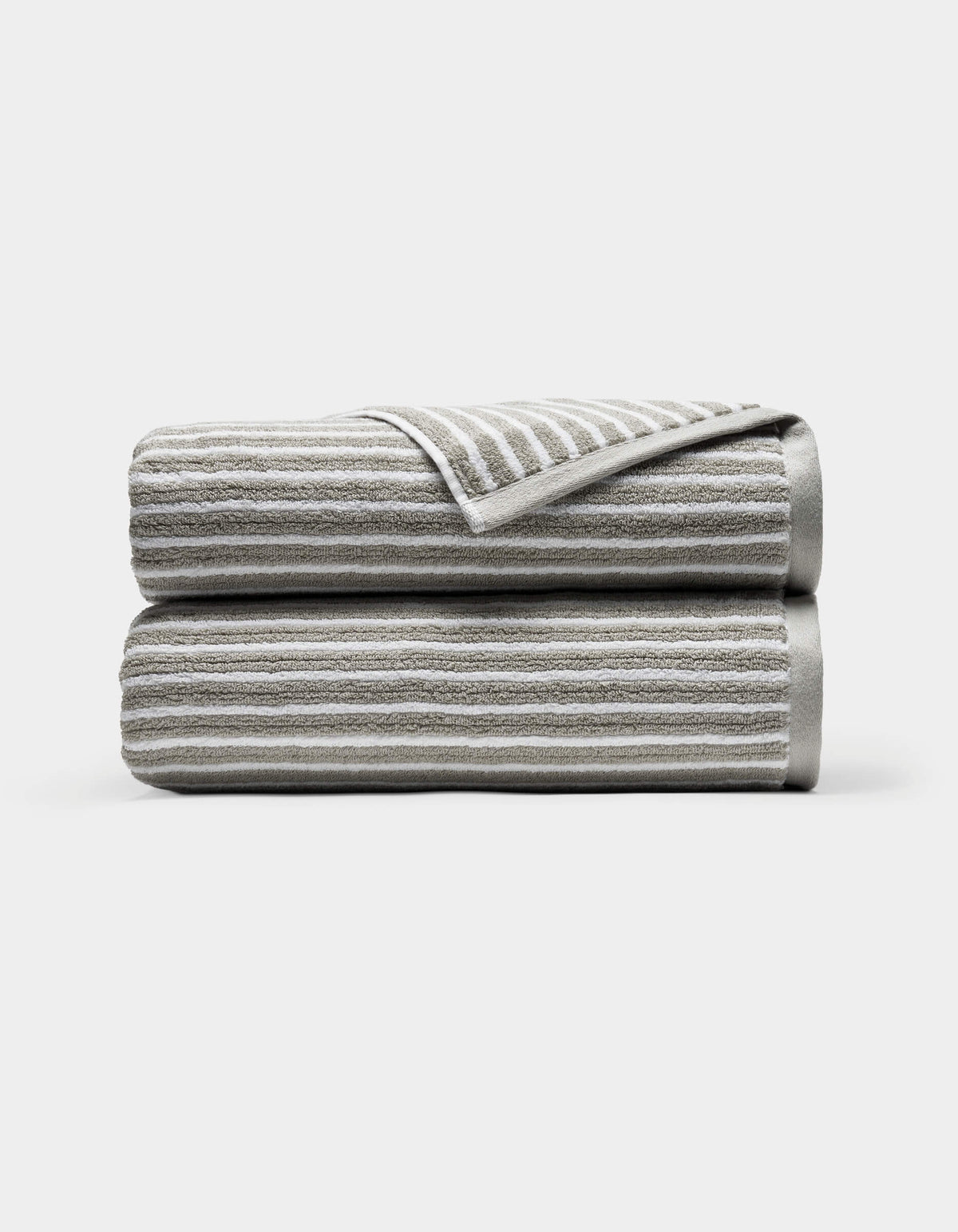 Two neatly folded Ribbed Terry Bath Towels by Cozy Earth, light gray with horizontal white stripes, stacked atop each other against a plain white background. A corner of the top towel is turned over, revealing the underside.