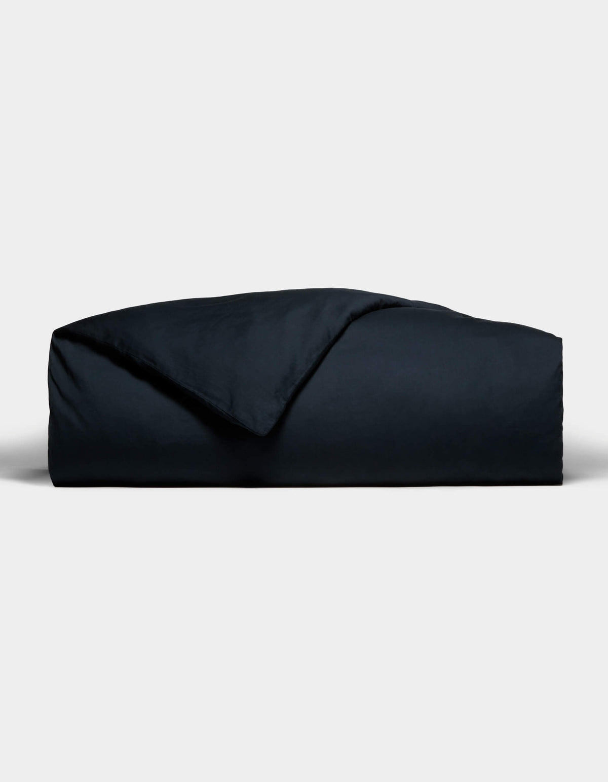 The Cozy Earth Soft-Wash Cotton Duvet Cover, in a dark hue, is neatly folded with one corner flipped to reveal its smooth texture, set against a plain light gray background.