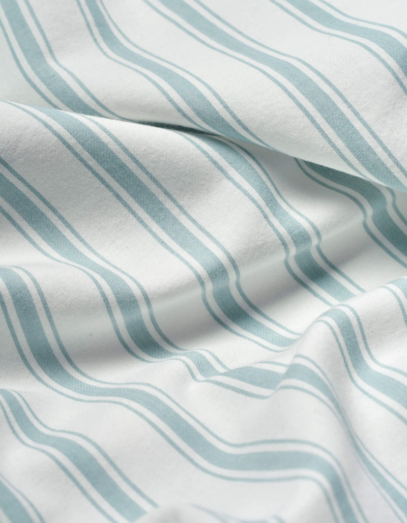 Close-up of Cozy Earth’s Soft-Wash Cotton Sheet Set in white, featuring light blue wavy parallel stripes. The soft fabric is slightly wrinkled, forming gentle folds and subtle shadows.