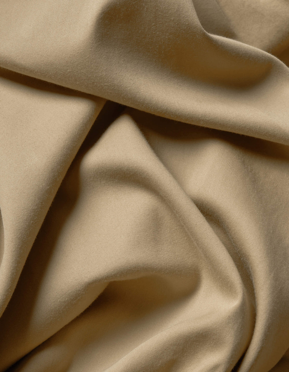 A close-up of Cozy Earth's Soft-Wash Cotton Flat Sheet showcases its soft beige fabric with smooth folds and gentle shadows, highlighting the luxurious texture and movement.
