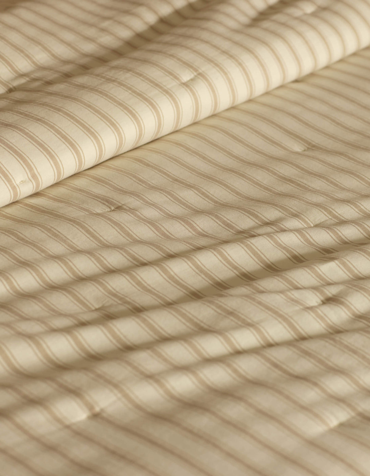 A close-up of the Cozy Earth Soft-Wash Cotton Quilt in beige shows its quilted fabric with thin horizontal stripes and gentle folds, highlighting its soft, textured look.