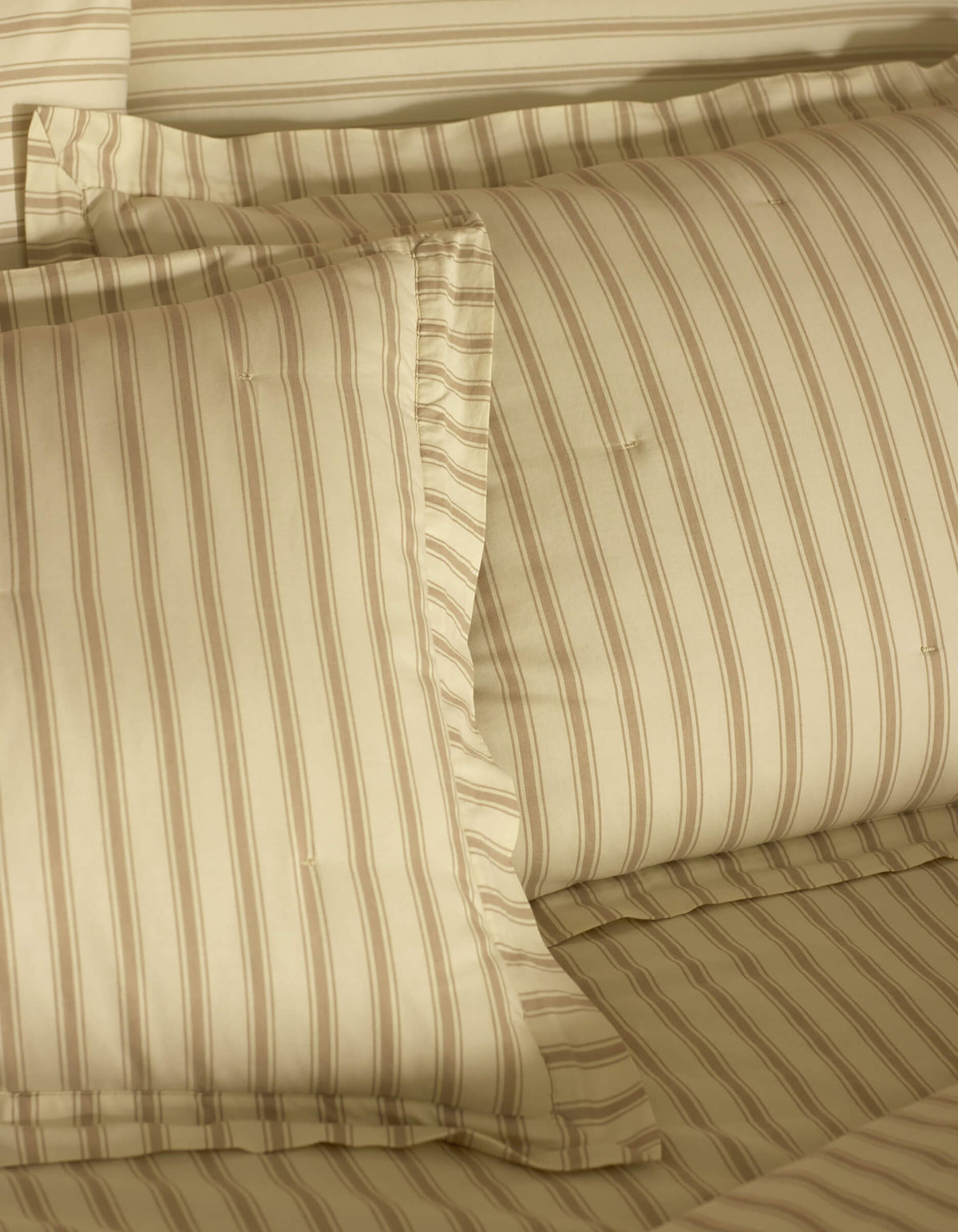 Close-up of a neatly made bed featuring Cozy Earth Soft-Wash Cotton Quilted Shams, showcasing smooth, soft fabric and subtle beige and light brown stripes on pillows and sheets for a cozy look.