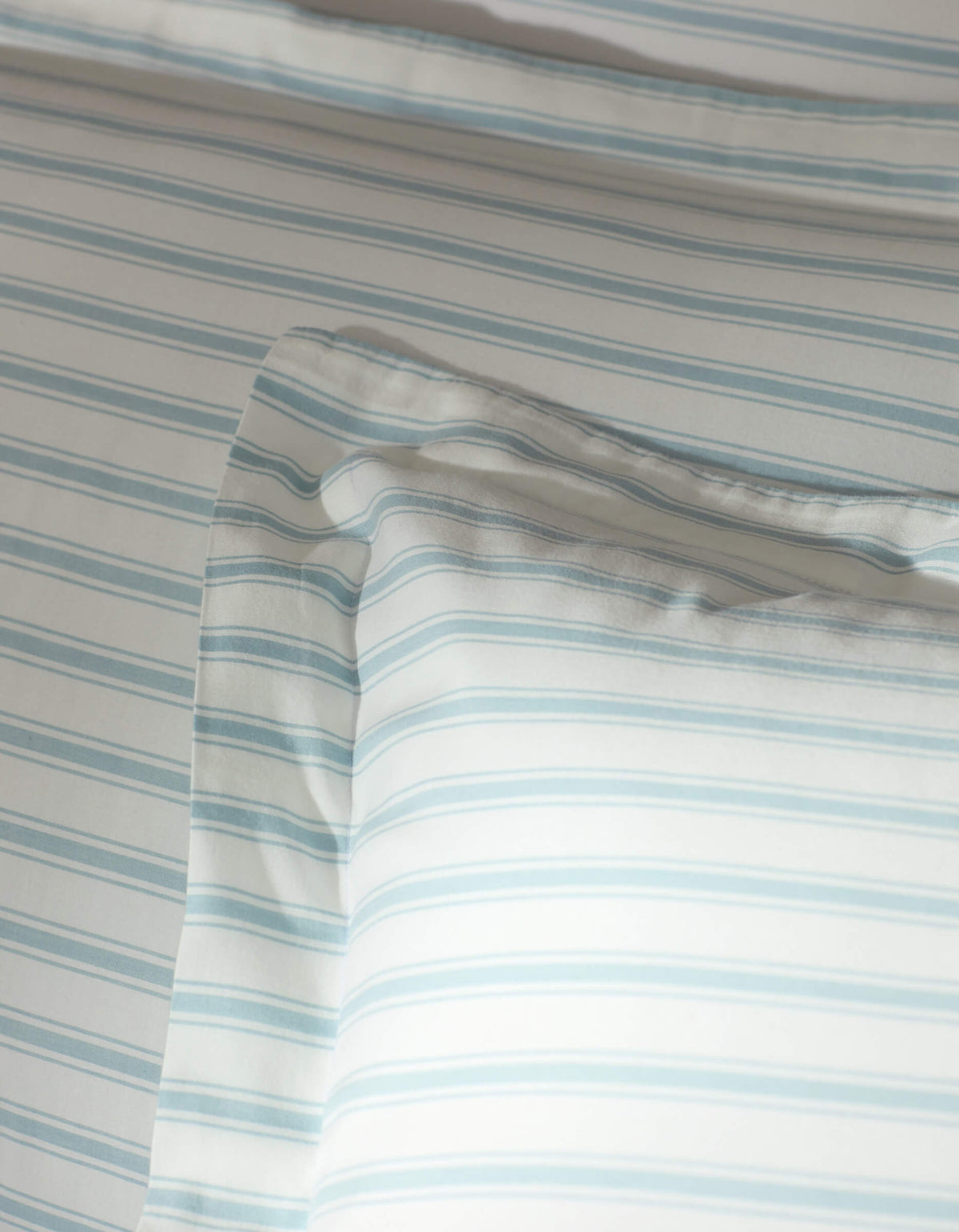 A close-up of a bed featuring Cozy Earth’s Soft-Wash Cotton Shams, dressed in white with thin, light blue stripes. The soft fabric and minimalist pattern create a calm, inviting look.