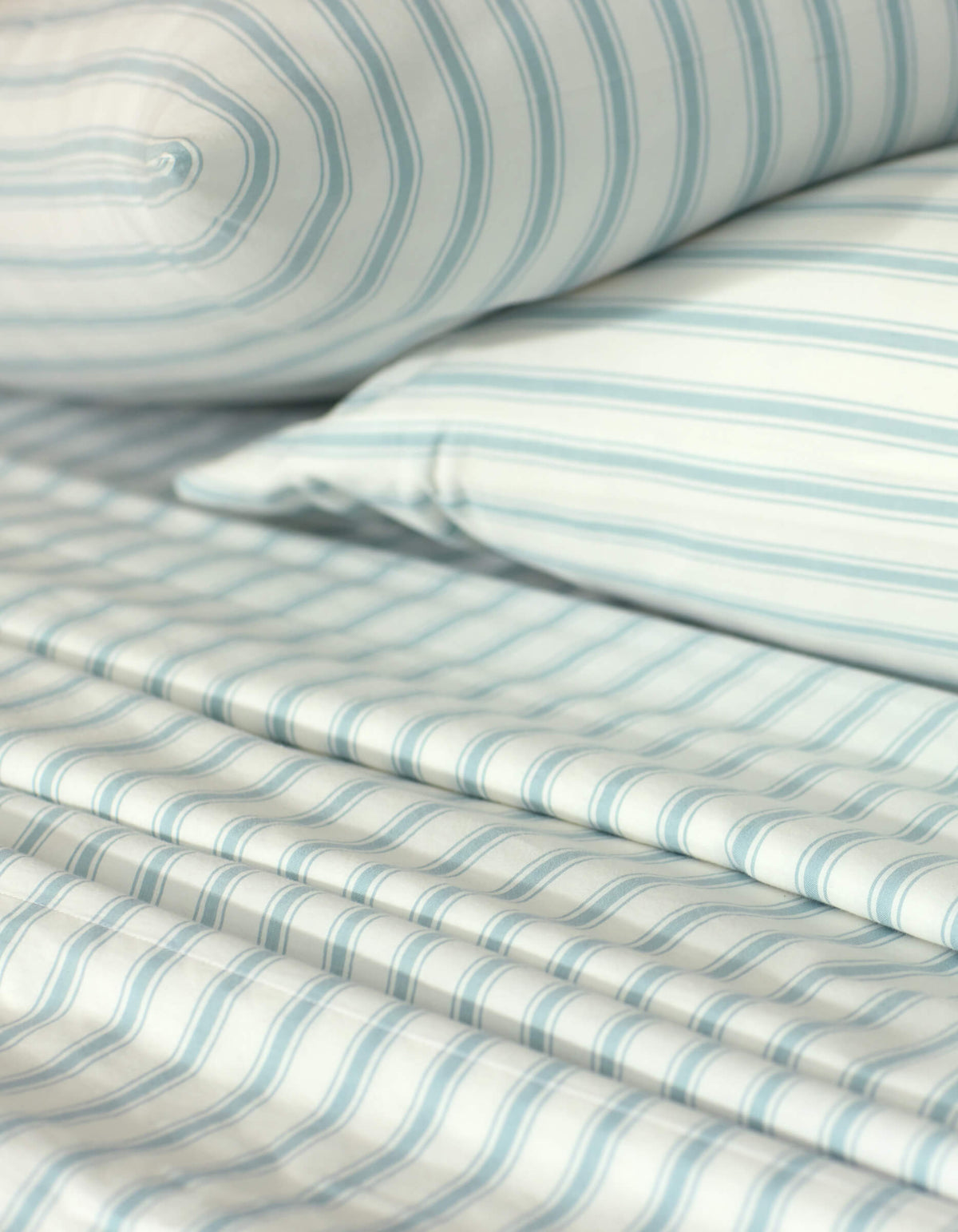 Close-up of a neatly made bed showcasing the Cozy Earth Soft-Wash Cotton Sheet Set, including a pillow, fitted sheet, and flat sheet in a light blue and white striped pattern. The smooth fabric looks exceptionally soft.