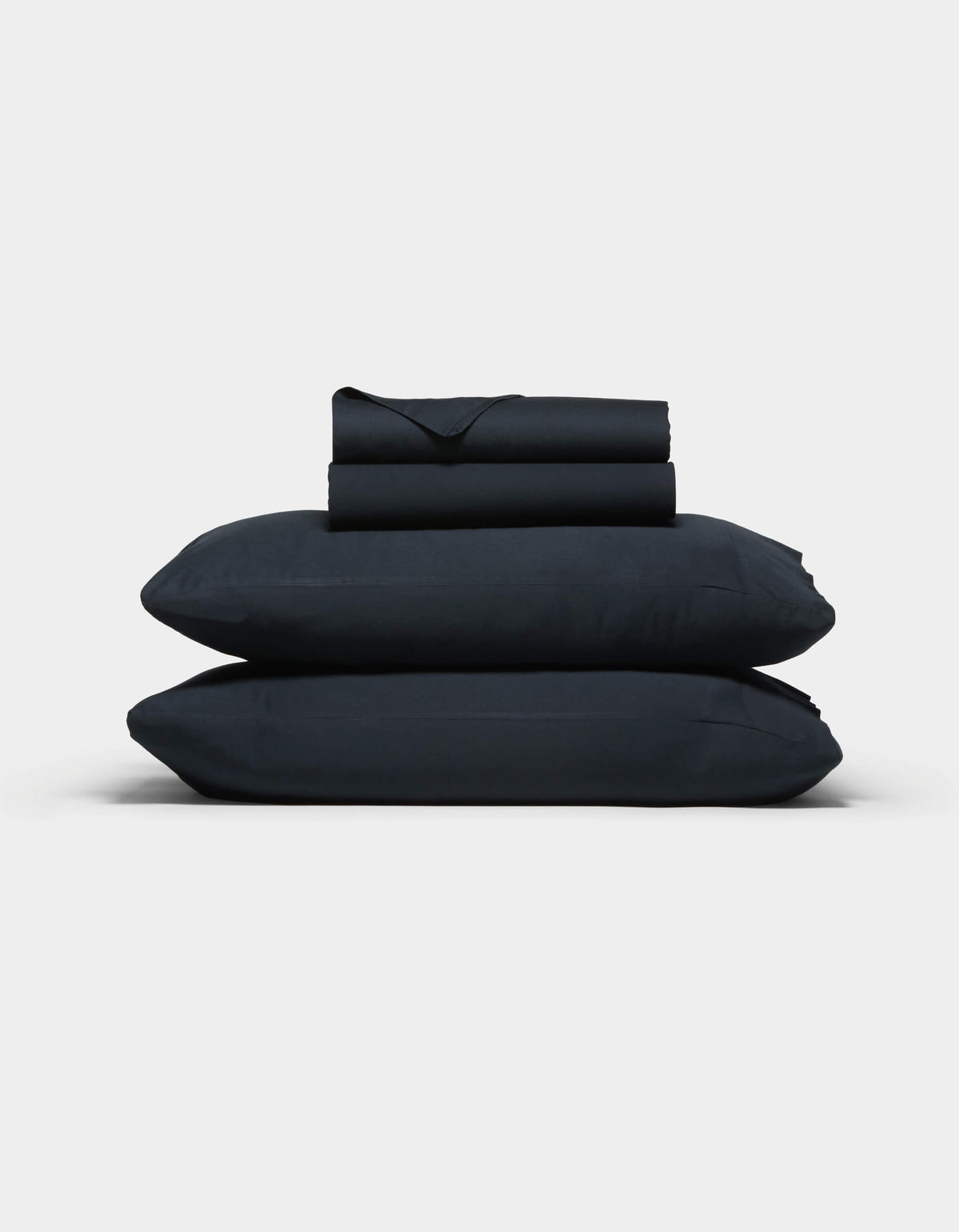 The Cozy Earth Soft-Wash Cotton Sheet Set, in dark navy blue, features two stacked pillows and folded sheets neatly arranged against a plain light gray background.