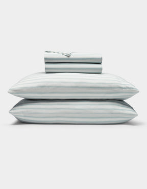 A neatly folded Soft-Wash Cotton Sheet Set by Cozy Earth in light blue and white stripes, featuring two stacked pillows and a folded fitted sheet, displayed on a plain white background.|Color:River and Sea Salt Stripe