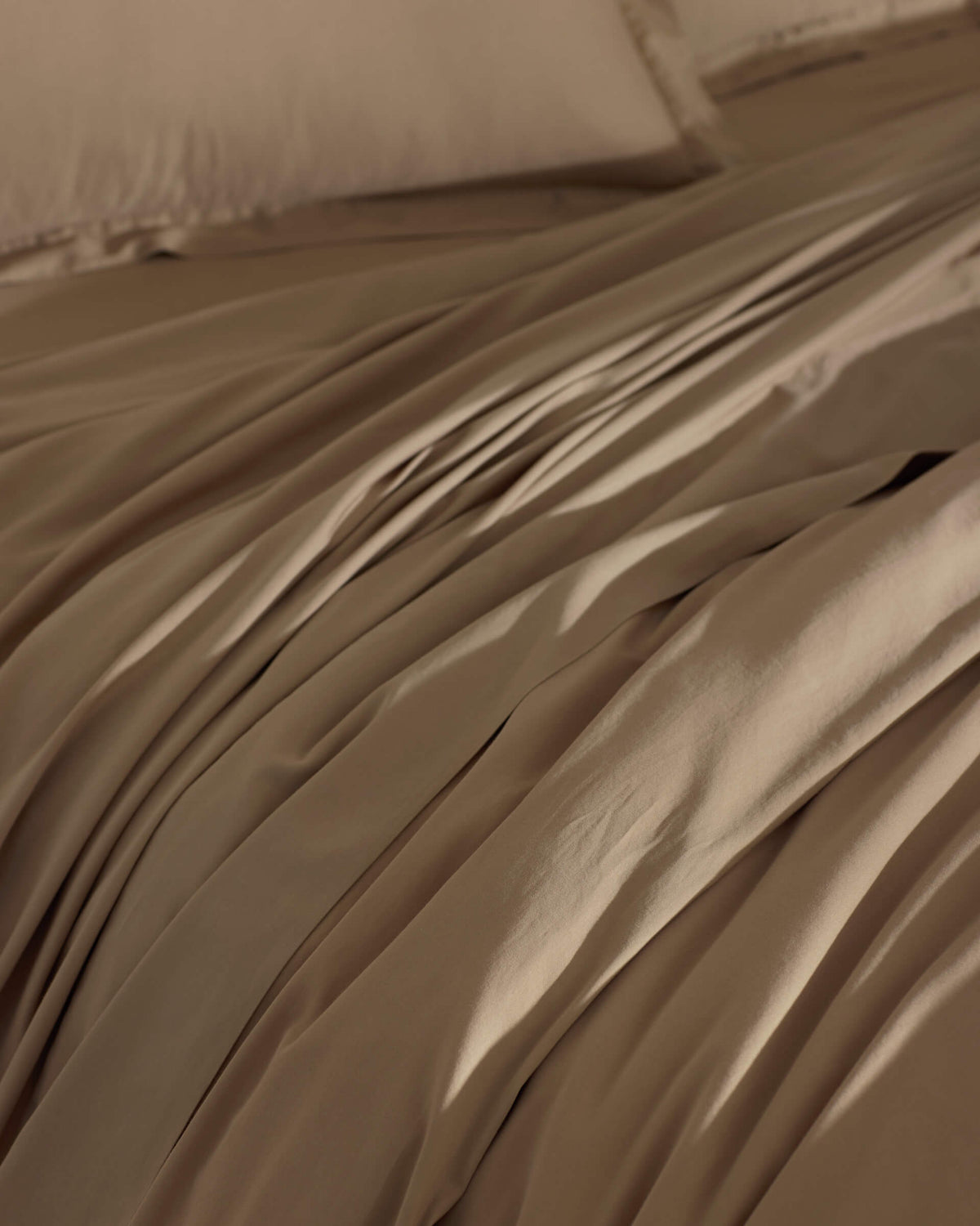 The Cozy Earth Soft-Wash Cotton Duvet Cover in brown is spread over the bed, creating gentle folds and shadows. Its smooth surface looks inviting, with matching pillowcases partially visible in the background.