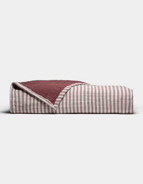The Cozy Earth Waterfront Coverlet, a folded quilt in red and white stripes with one corner flipped to reveal a solid dark red underside, is displayed against a plain white background.|Color:Currant Stripe