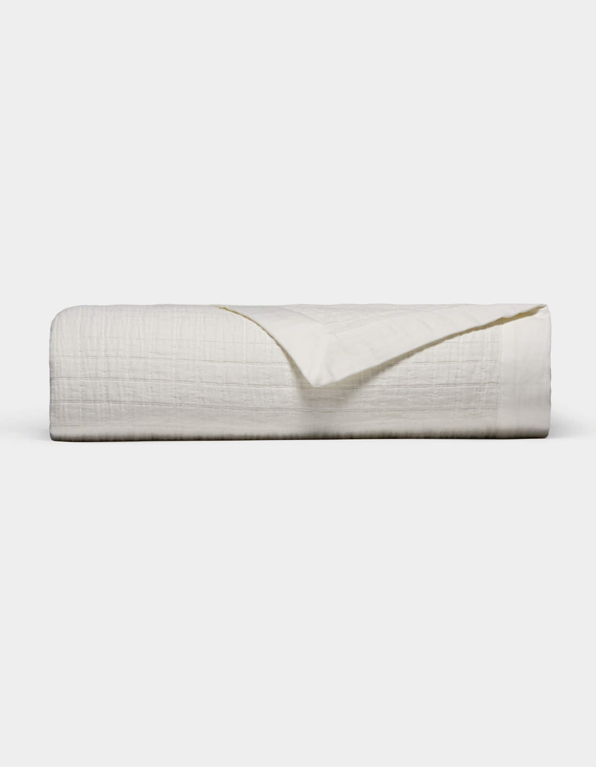 The Waterfront Grid Matelasse Blanket by Cozy Earth is shown neatly folded with a textured, crinkled surface against a plain light background. One corner is flipped over to reveal the underside.