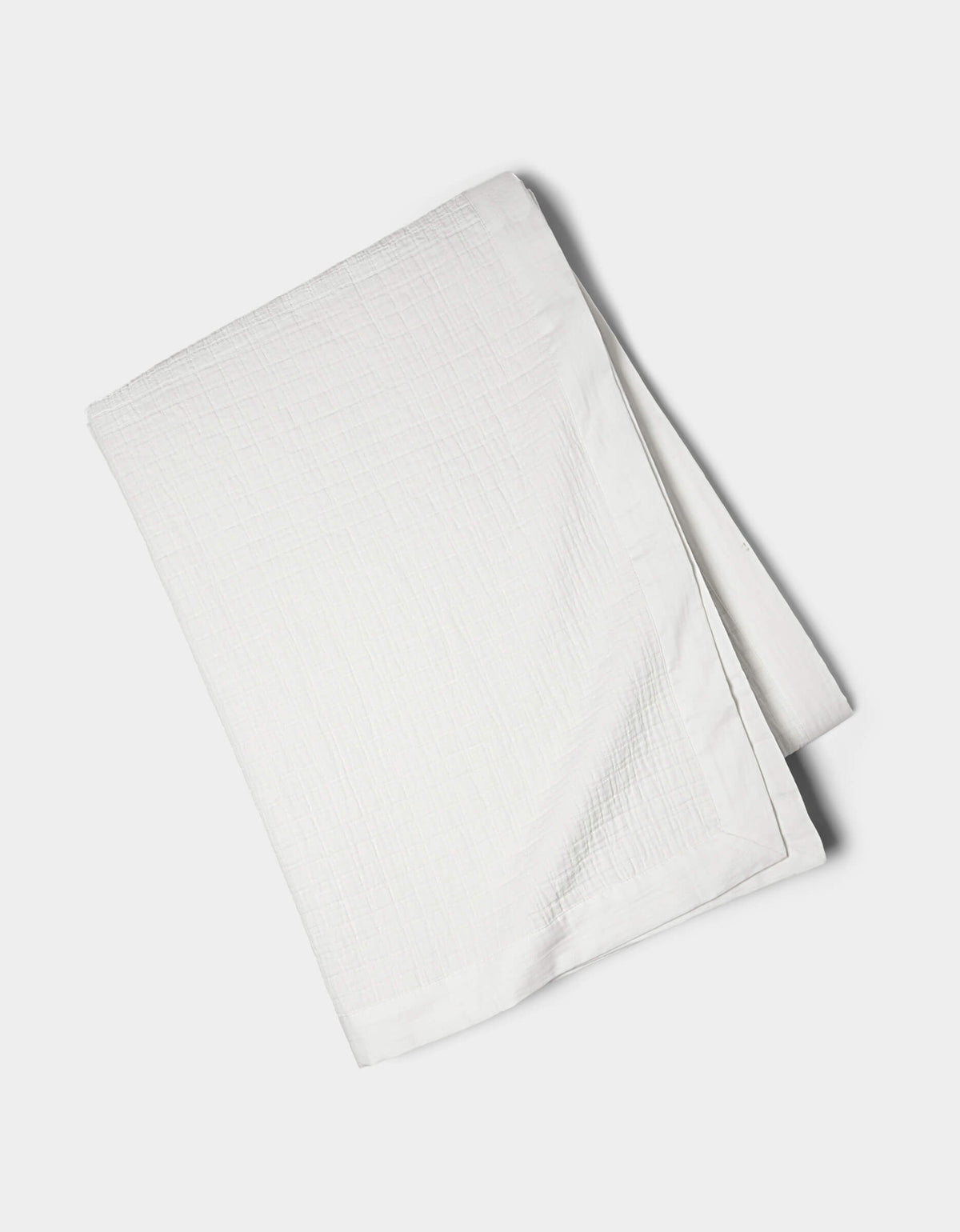 The Cozy Earth Waterfront Grid Matelasse Blanket, in white with a textured design, is neatly folded on a plain, light-colored surface.