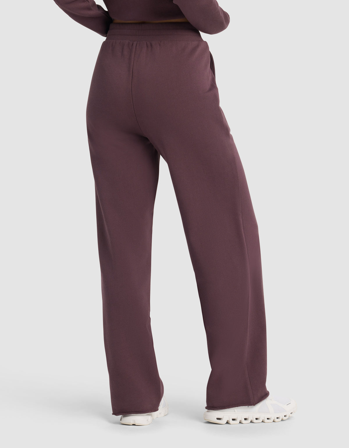 A person is shown from the back wearing Cozy Earth's Chelsea Pant in maroon, a loose-fitting, high-waisted style, paired with white sneakers and arms at their sides.