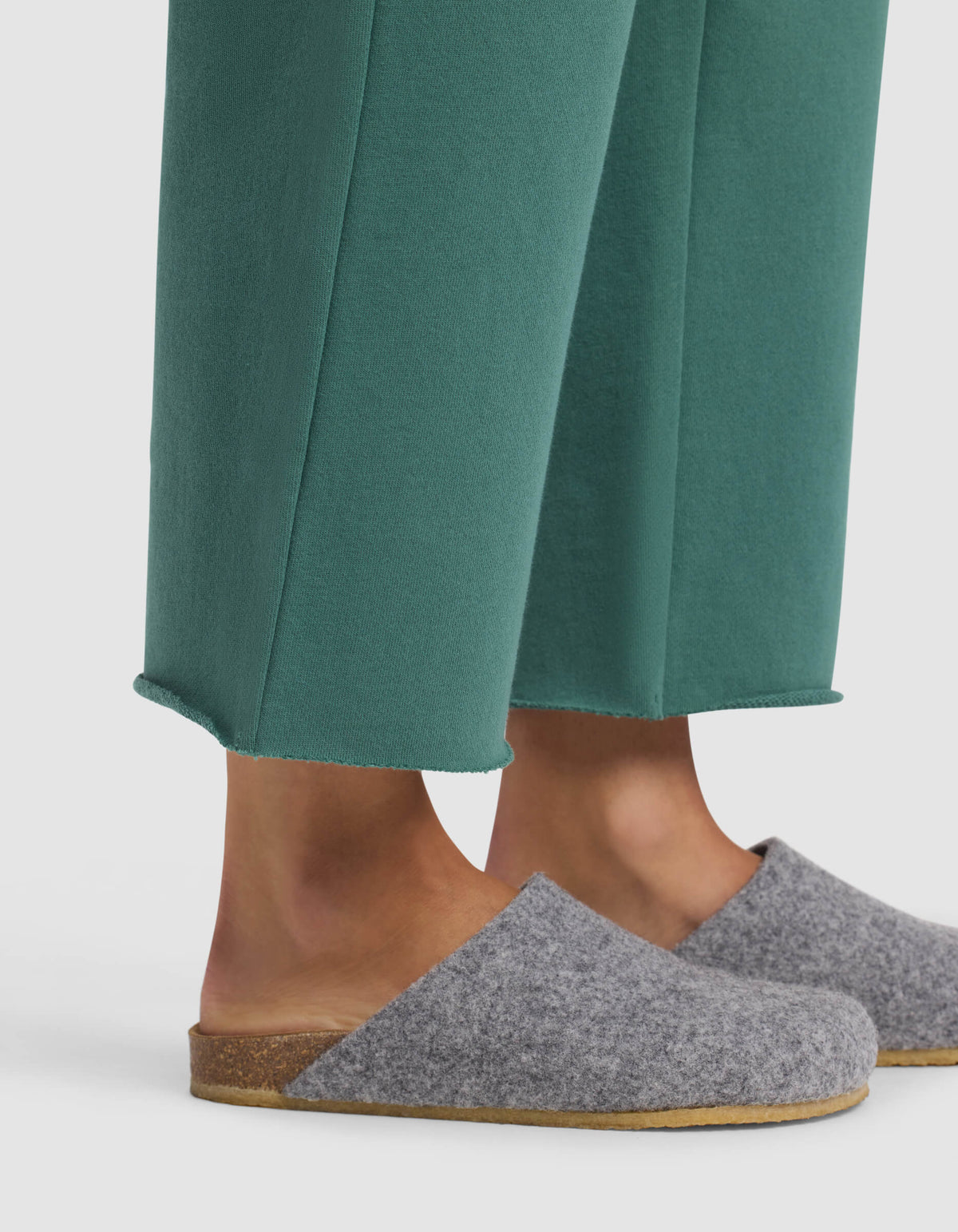 A person wearing Cozy Earth's Women's Chelsea Cropped Pant in green and gray wool slip-on slippers with cork soles, standing against a white background.