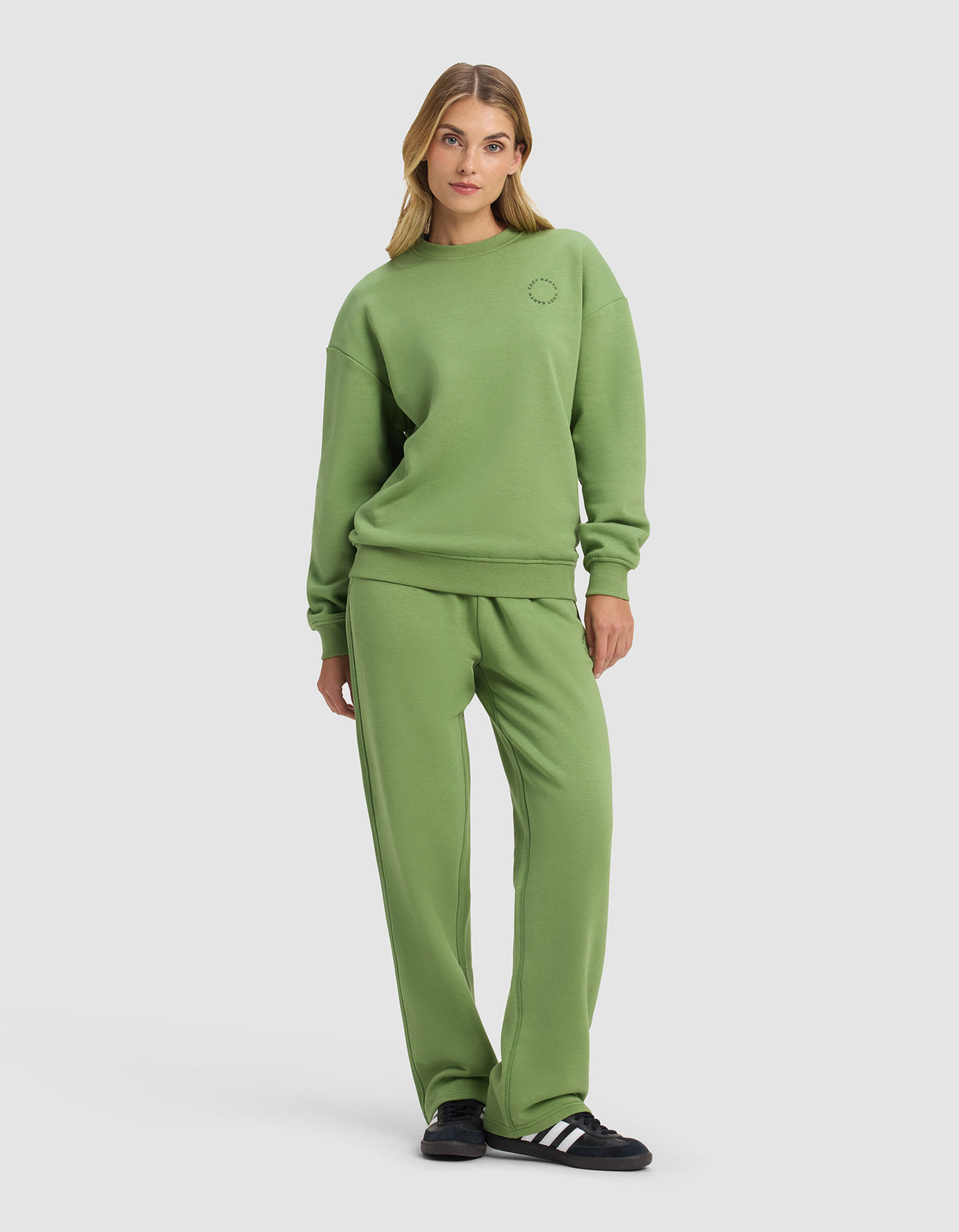 A woman poses casually in the Cozy Earth Women's Cityscape Crewneck & Wide Leg Pant Set, featuring a relaxed fit. She stands against a plain background with one hand in her pocket, completing the look with black and white sneakers.