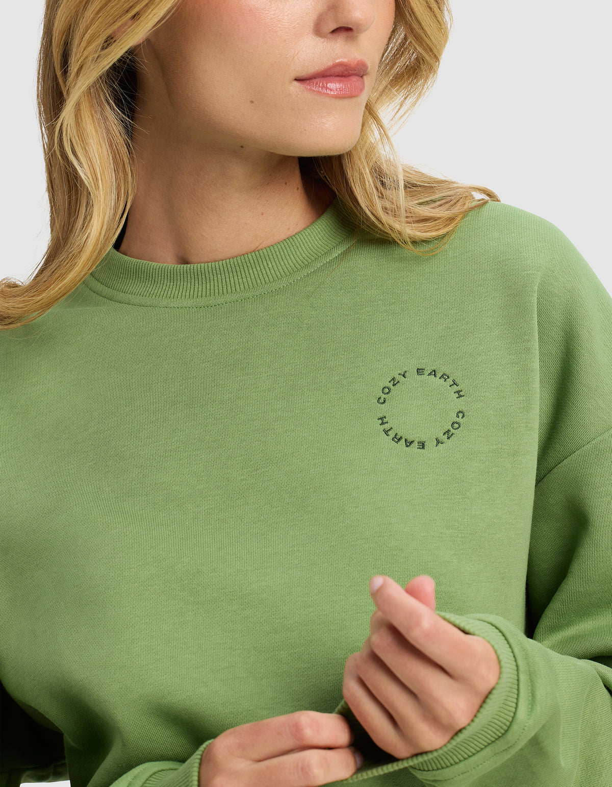 A woman wearing the Cozy Earth Women's Cityscape Crewneck in light green poses against a plain background, facing slightly to the side with her hand near her collar.