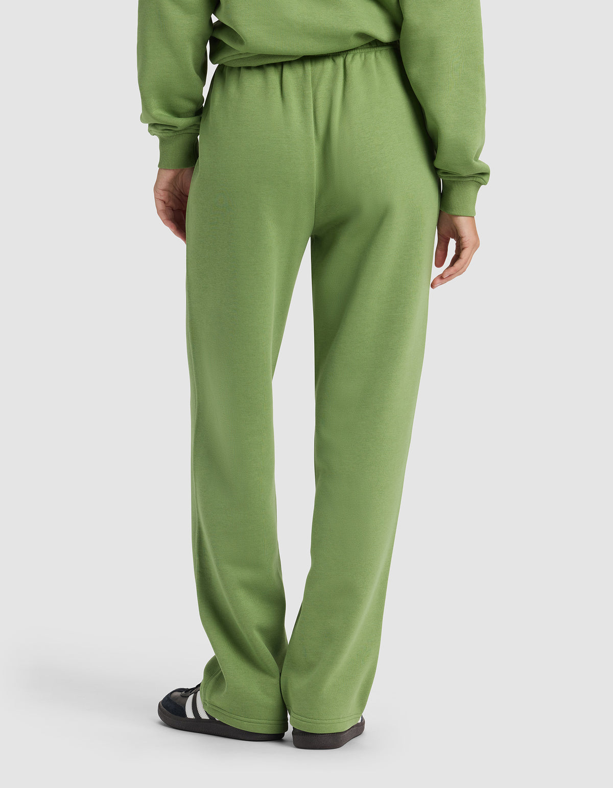 A person is seen from the back wearing the Cozy Earth Women's Cityscape Wide Leg Pant in light green with a matching sweatshirt and black sandals with white stripes, set against a plain, light-colored background.