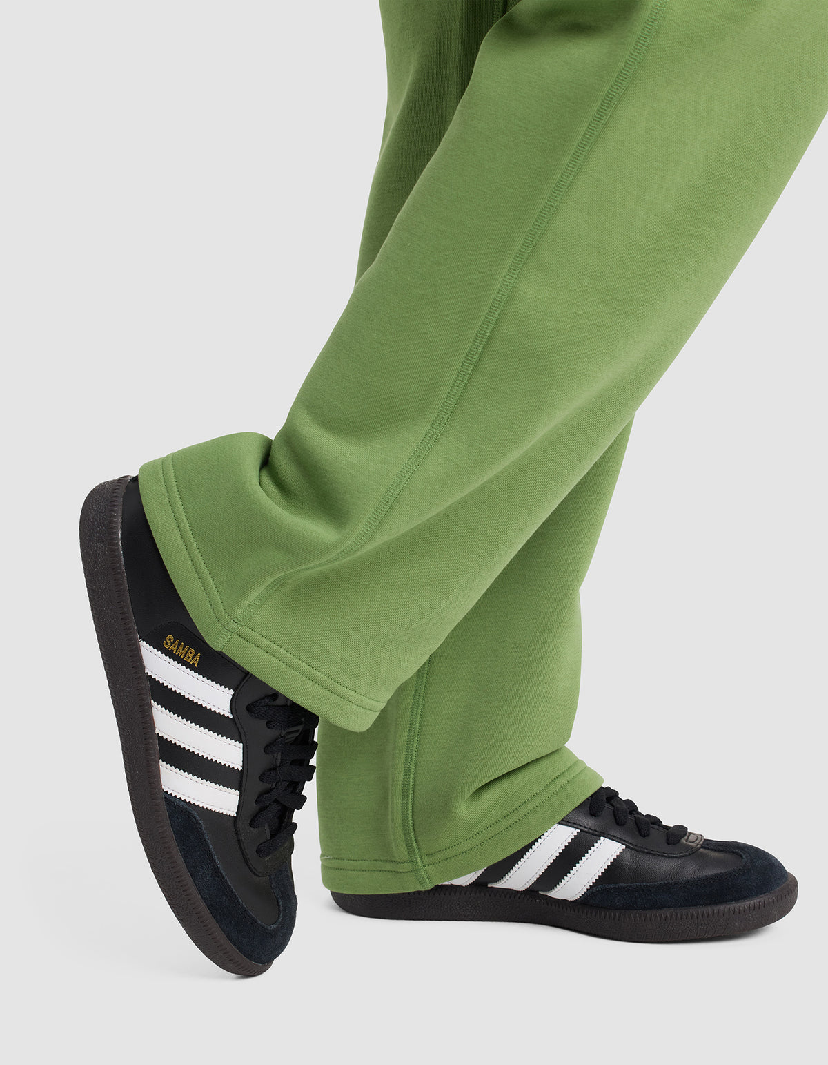 A person wearing Cozy Earth Women's Cityscape Wide Leg Pants and black Adidas Samba sneakers with white stripes stands with one foot crossed over the other on a light grey background.