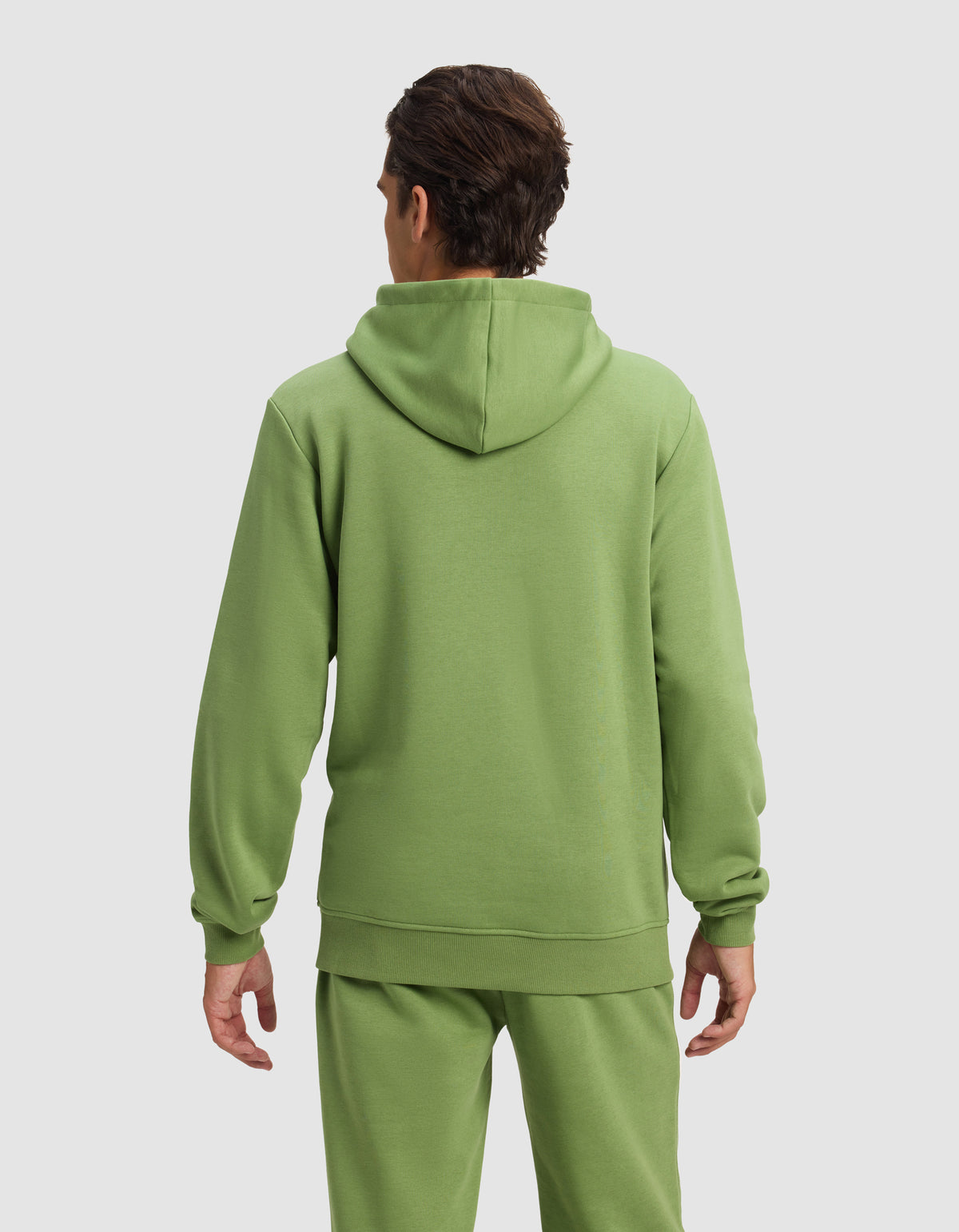 A man with short brown hair is seen from behind wearing the Cozy Earth Men's Cityscape Hoodie in light green, paired with matching sweatpants, standing against a plain light gray background.