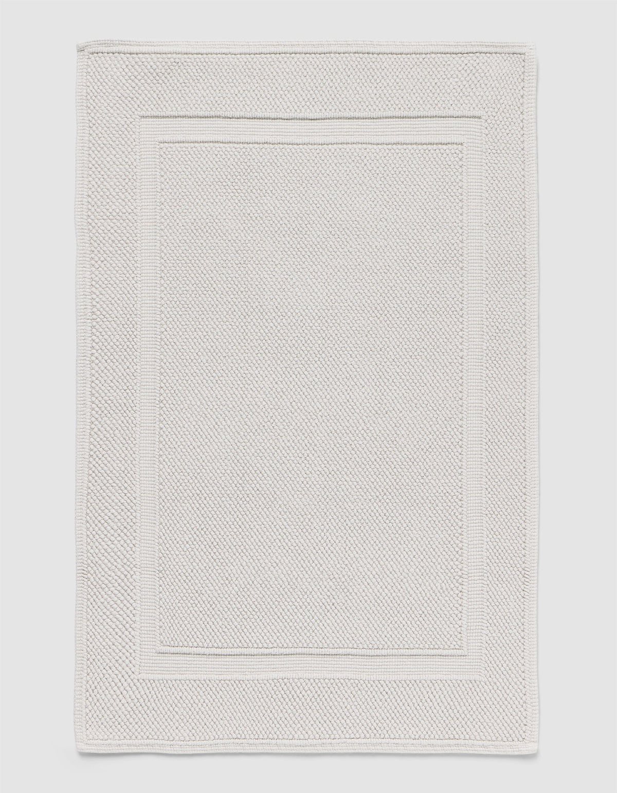 The Cozy Earth Classic Bath Mat features a rectangular shape, light color, subtle textured pattern, and elegant double border design on the edges.
