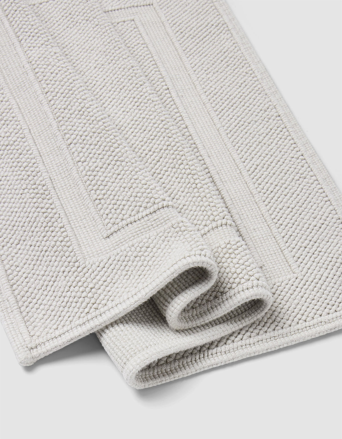 The Cozy Earth Classic Bath Mat is a folded light grey, textured mat with a rectangular border pattern, displayed on a white background.