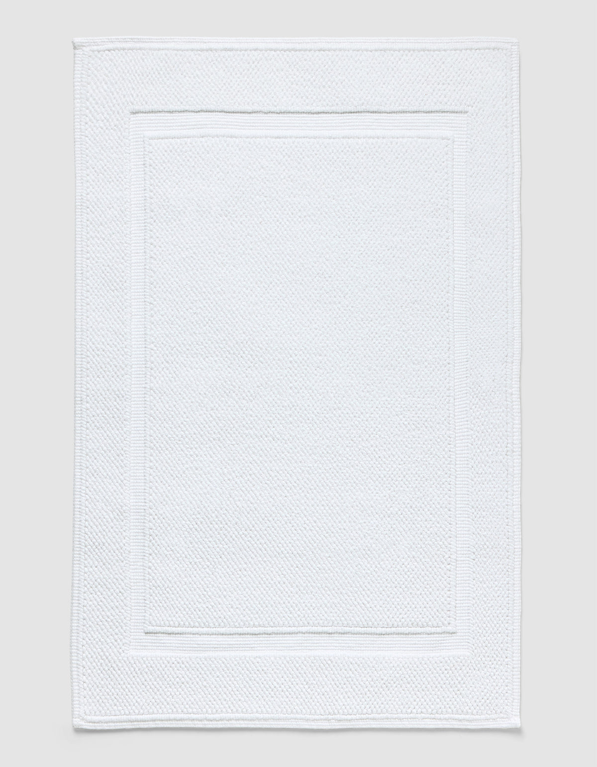 The Cozy Earth Classic Bath Mat in white features a textured surface with a subtle border pattern and is shown flat against a neutral background.