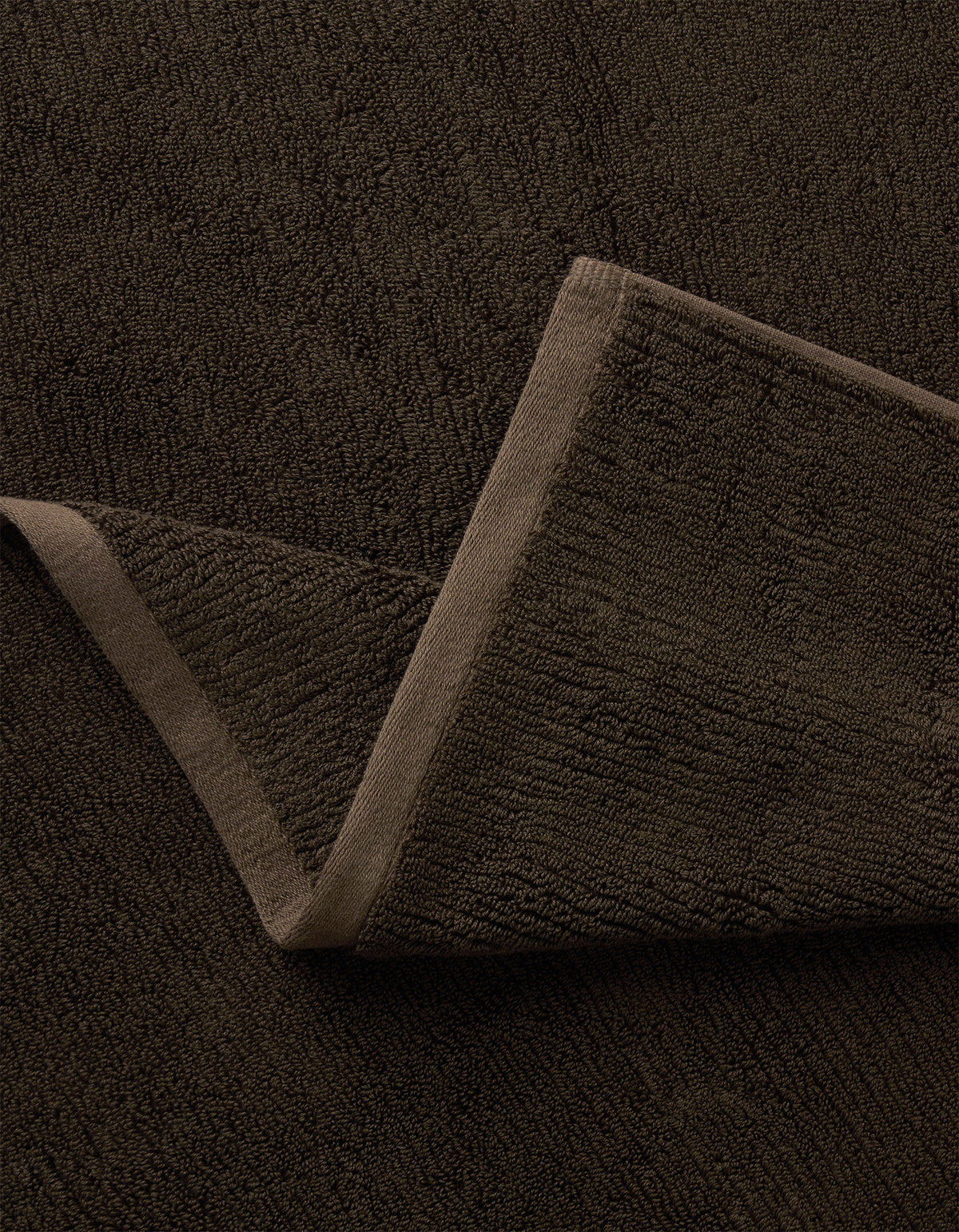 A close-up of the Complete Ribbed Terry Bath Bundle by Cozy Earth in dark brown, featuring one corner folded to reveal its soft ribbed fabric and stitched edges.